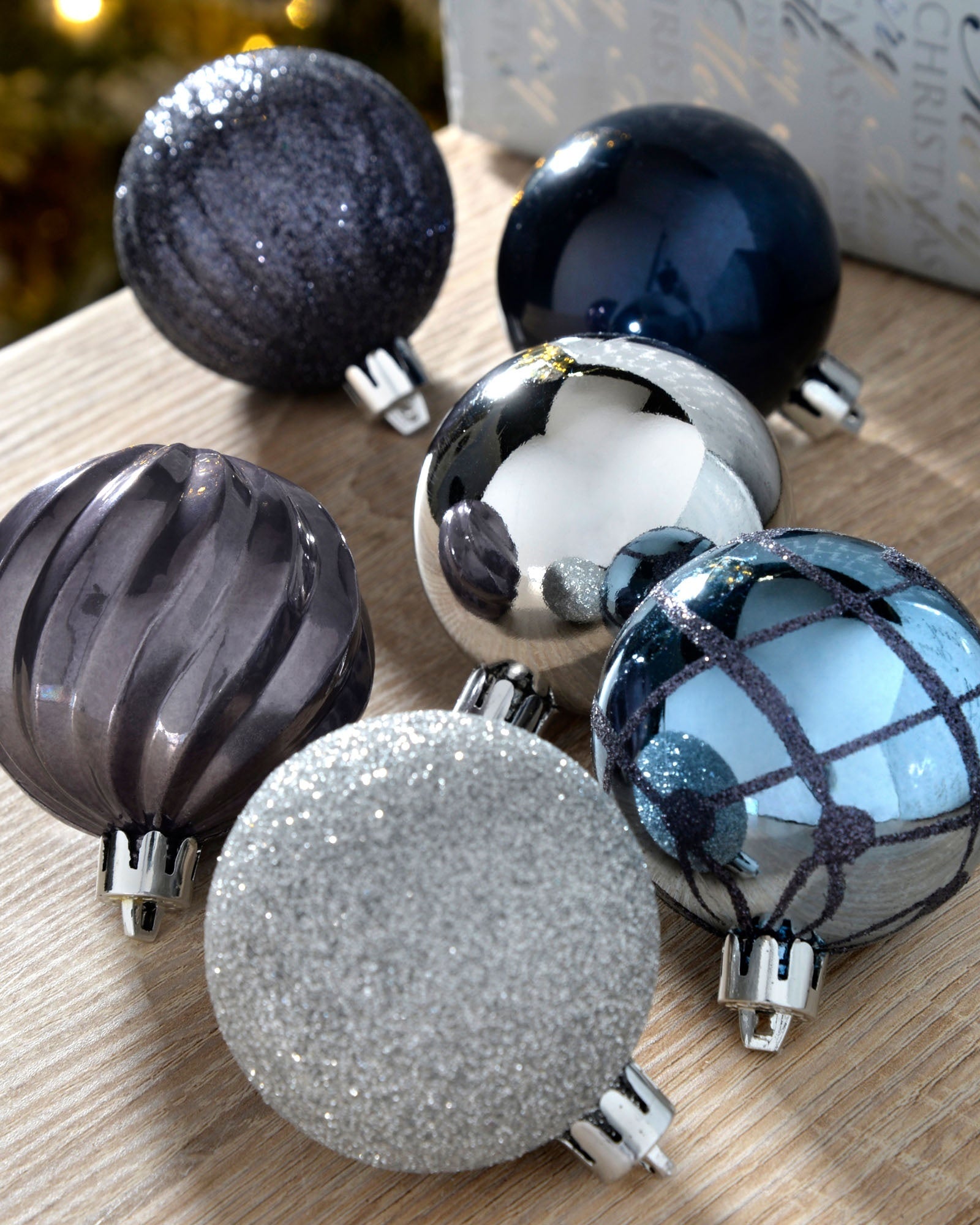 Navy, silver and grey 6cm shatterproof baubles with glitter, mirrored and patterned finishes on a wooden surface