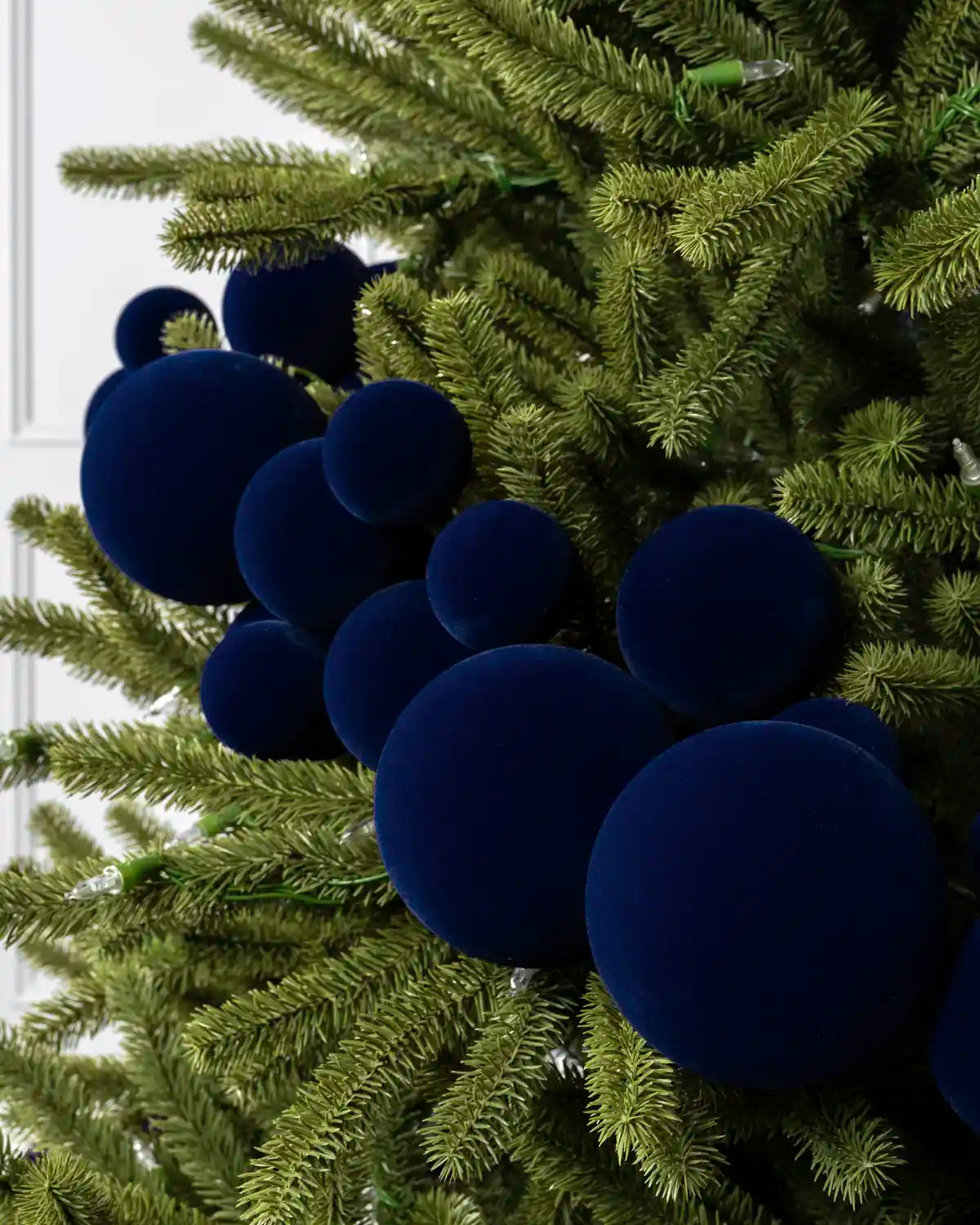 Close-up of navy velvet bauble garland on a Christmas tree showing the soft textured finish and mixed bauble sizes.
