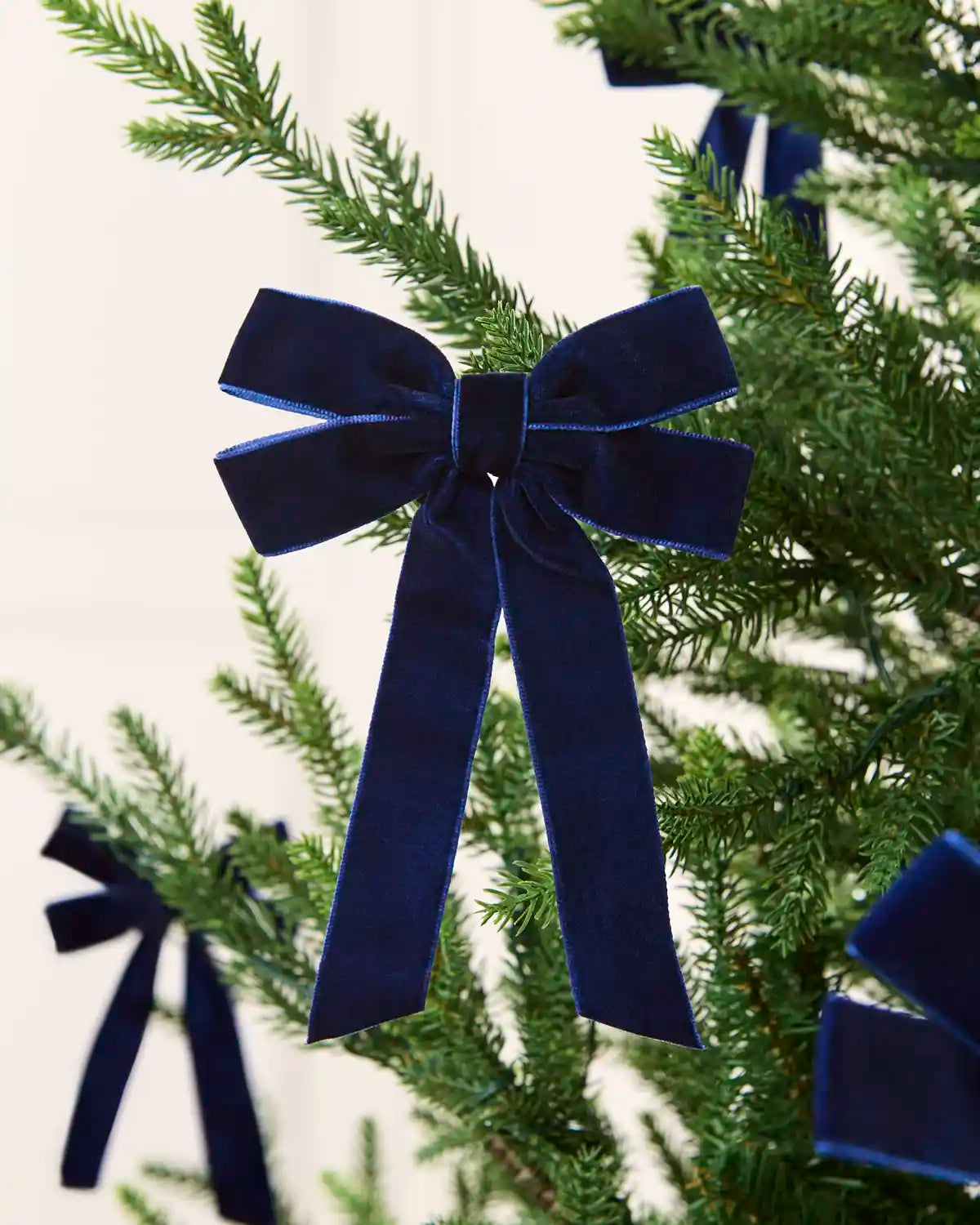 Navy velvet double bow displayed among multiple matching bows on a Christmas tree.