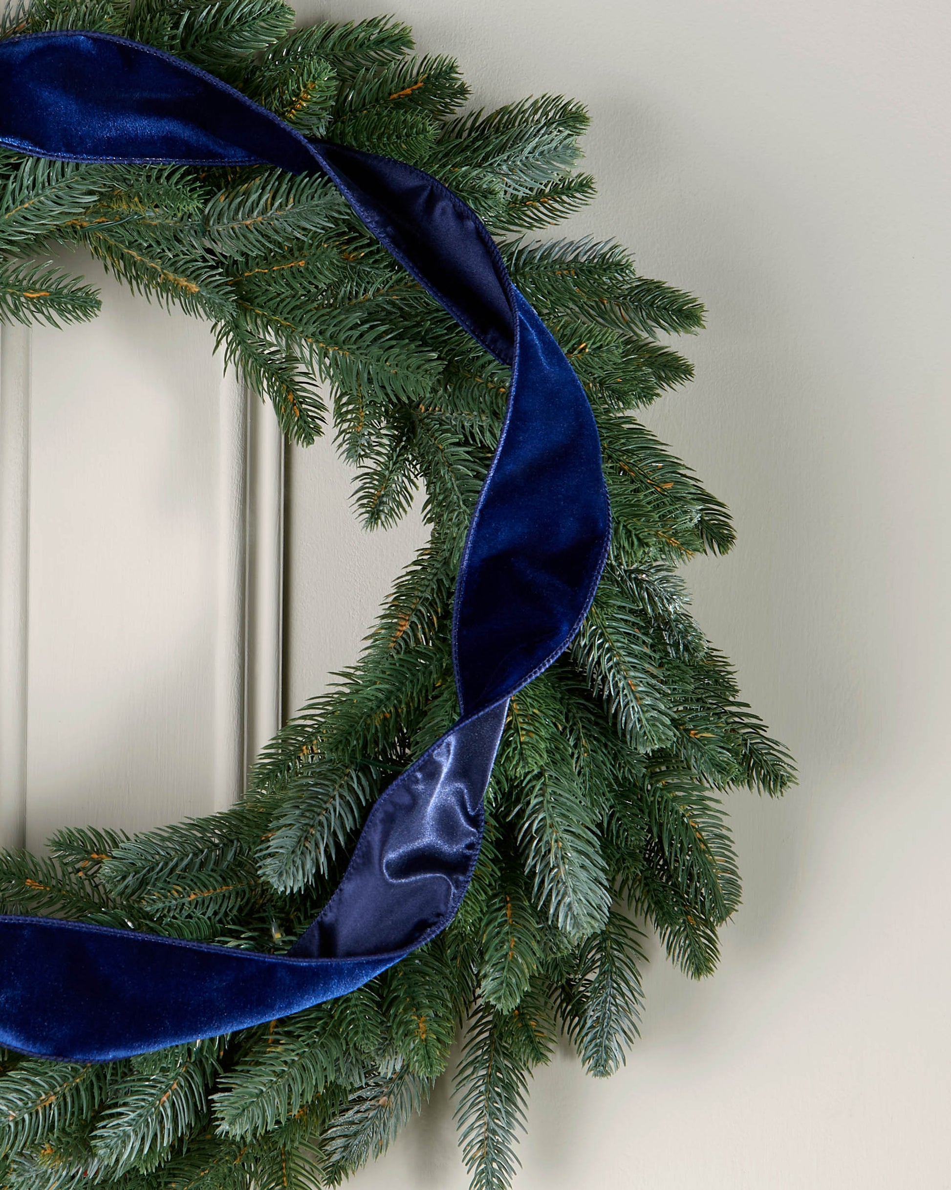 Navy velvet ribbon styled in a loose spiral on a green Christmas wreath.