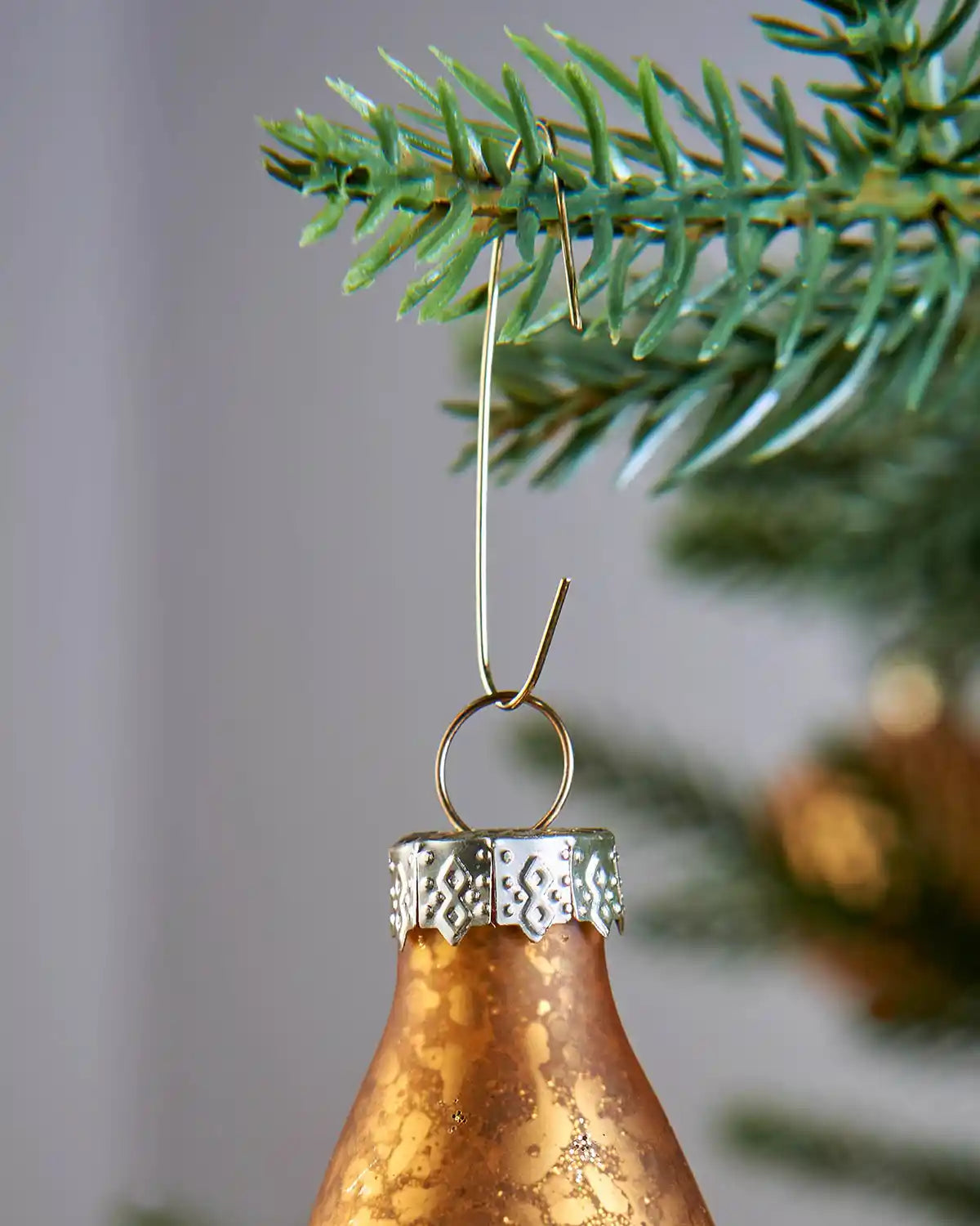 Gold ornament hook hanging from a Christmas tree branch with a bauble attached