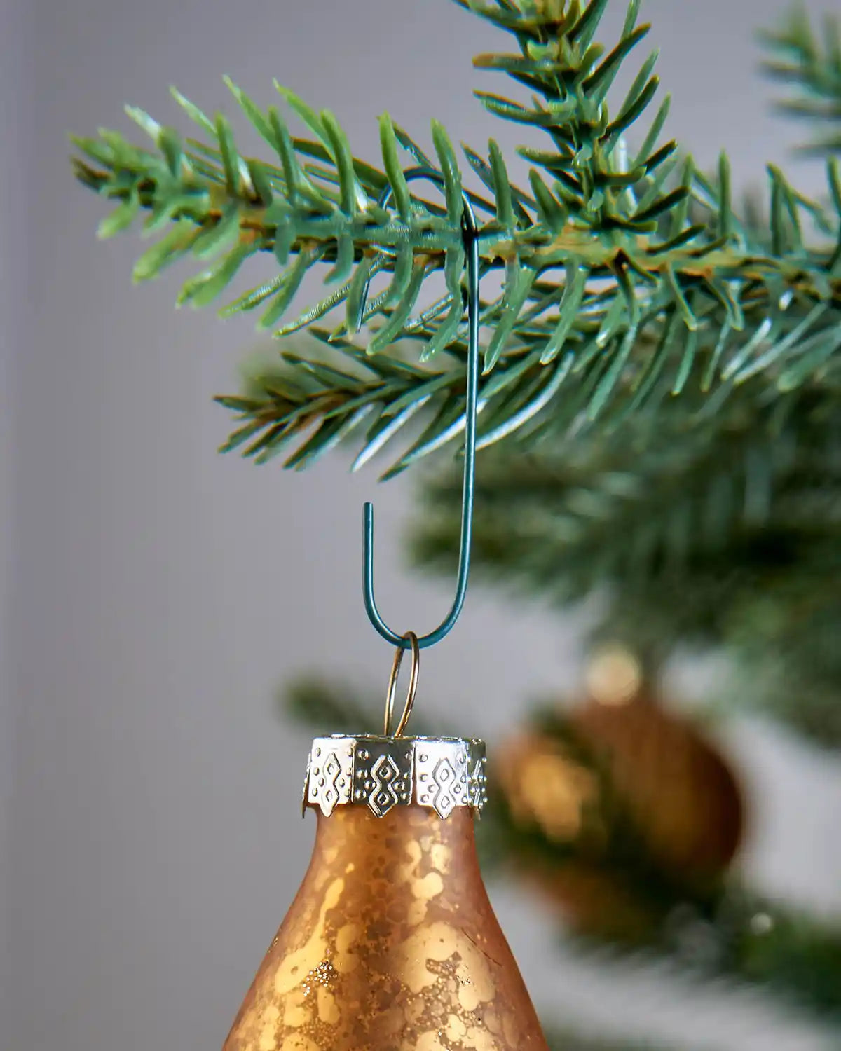 Green ornament hook hanging from a Christmas tree branch with a bauble attached