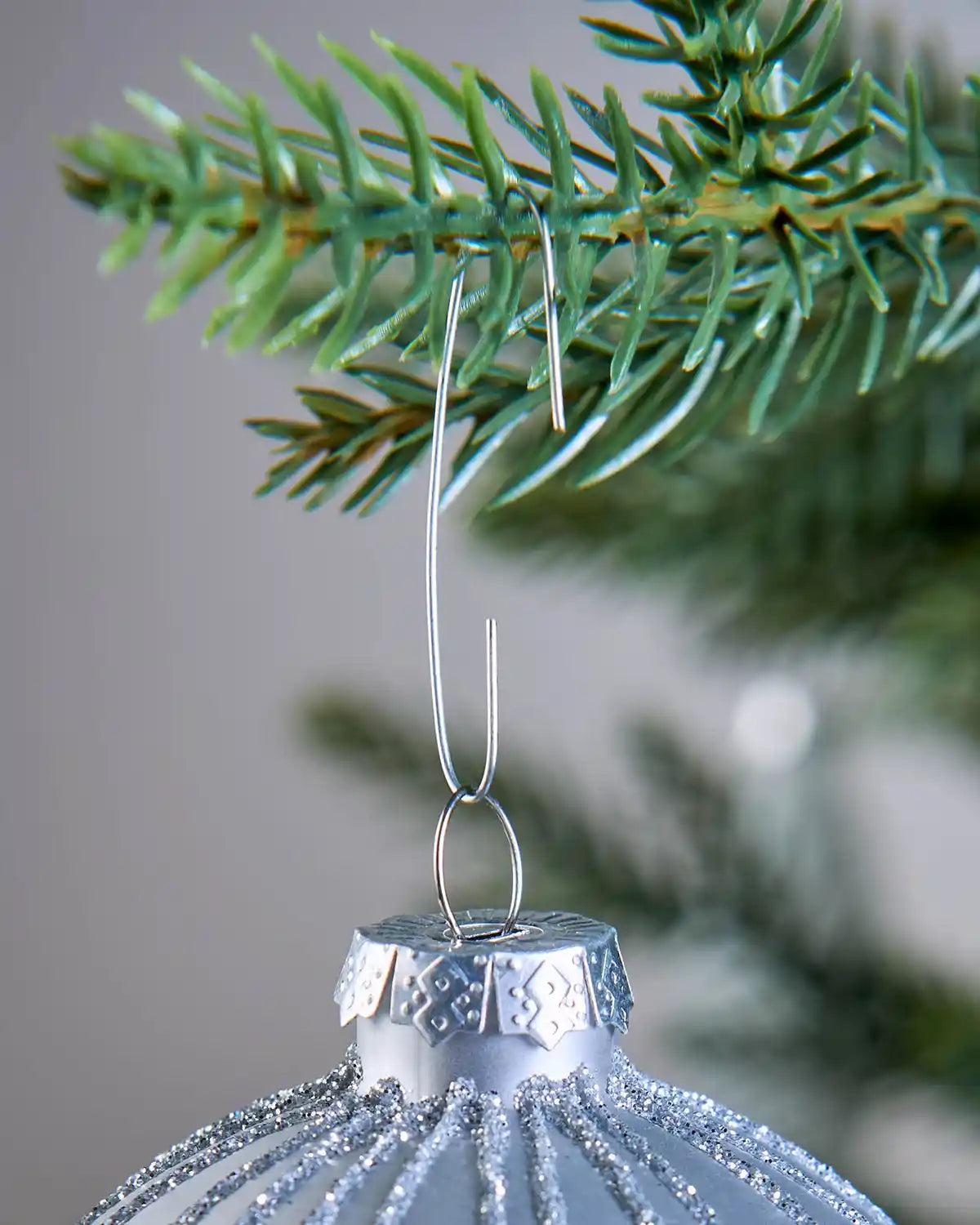 Silver ornament hook hanging from a Christmas tree branch with a bauble attached