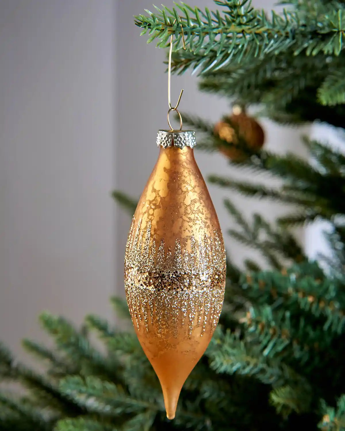 Gold bauble ornament hook securing a copper Christmas bauble to a tree branch