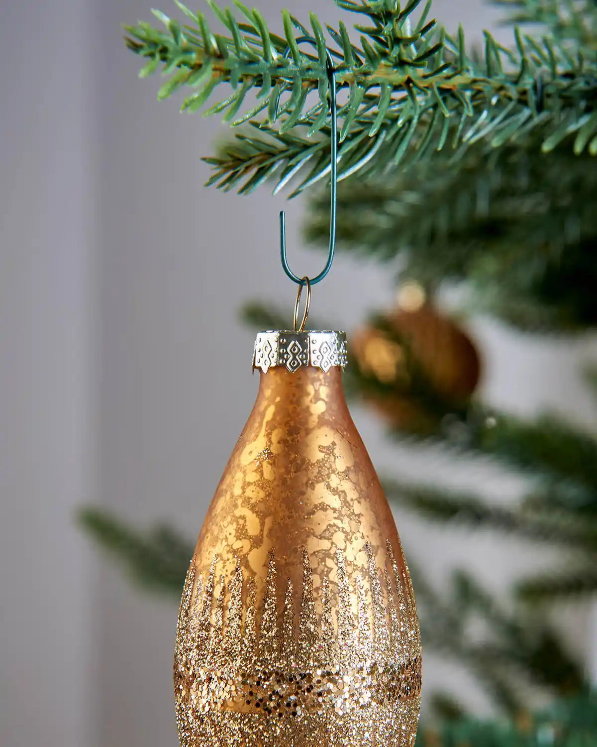 Green bauble ornament hook securing a copper Christmas bauble to a tree branch