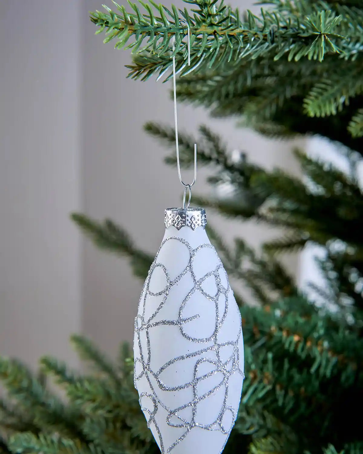 Close-up of a white Christmas ornament hanging from a silver bauble hook on a tree branch