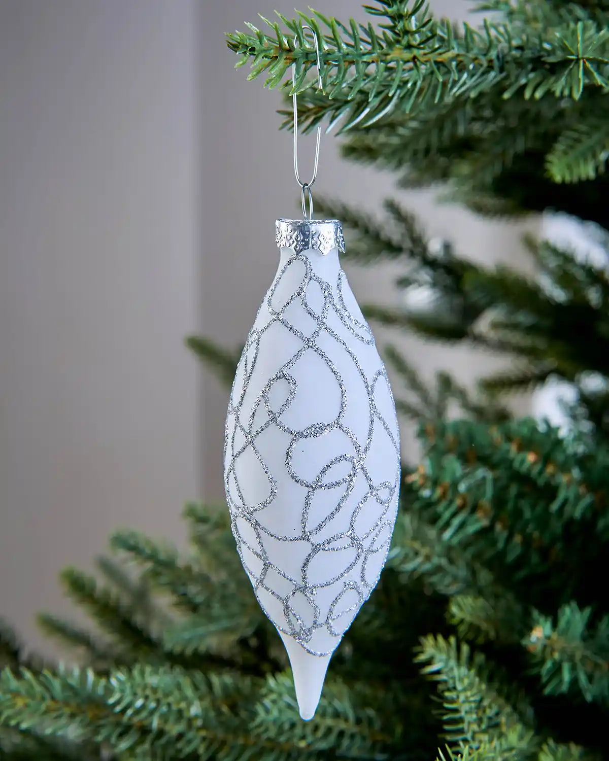White Christmas ornament hanging from a silver bauble hook on a tree branch