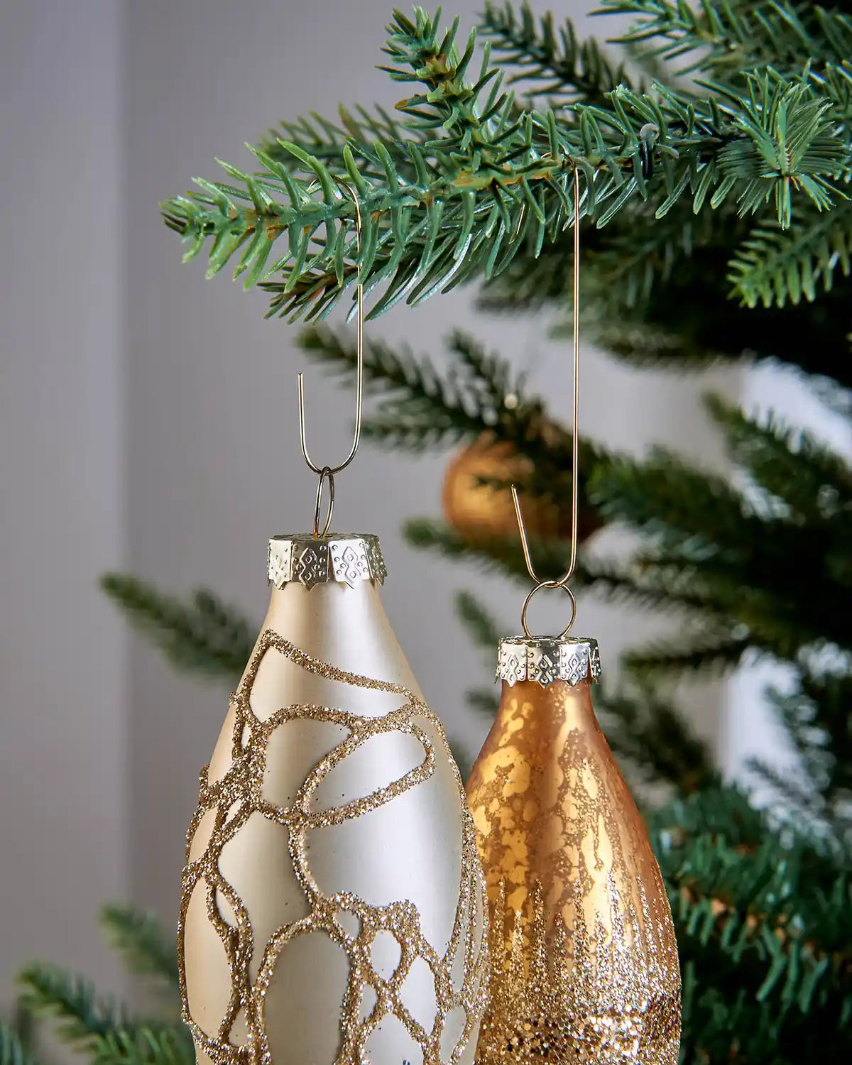 Gold ornament hooks hanging two decorative baubles from a Christmas tree branch