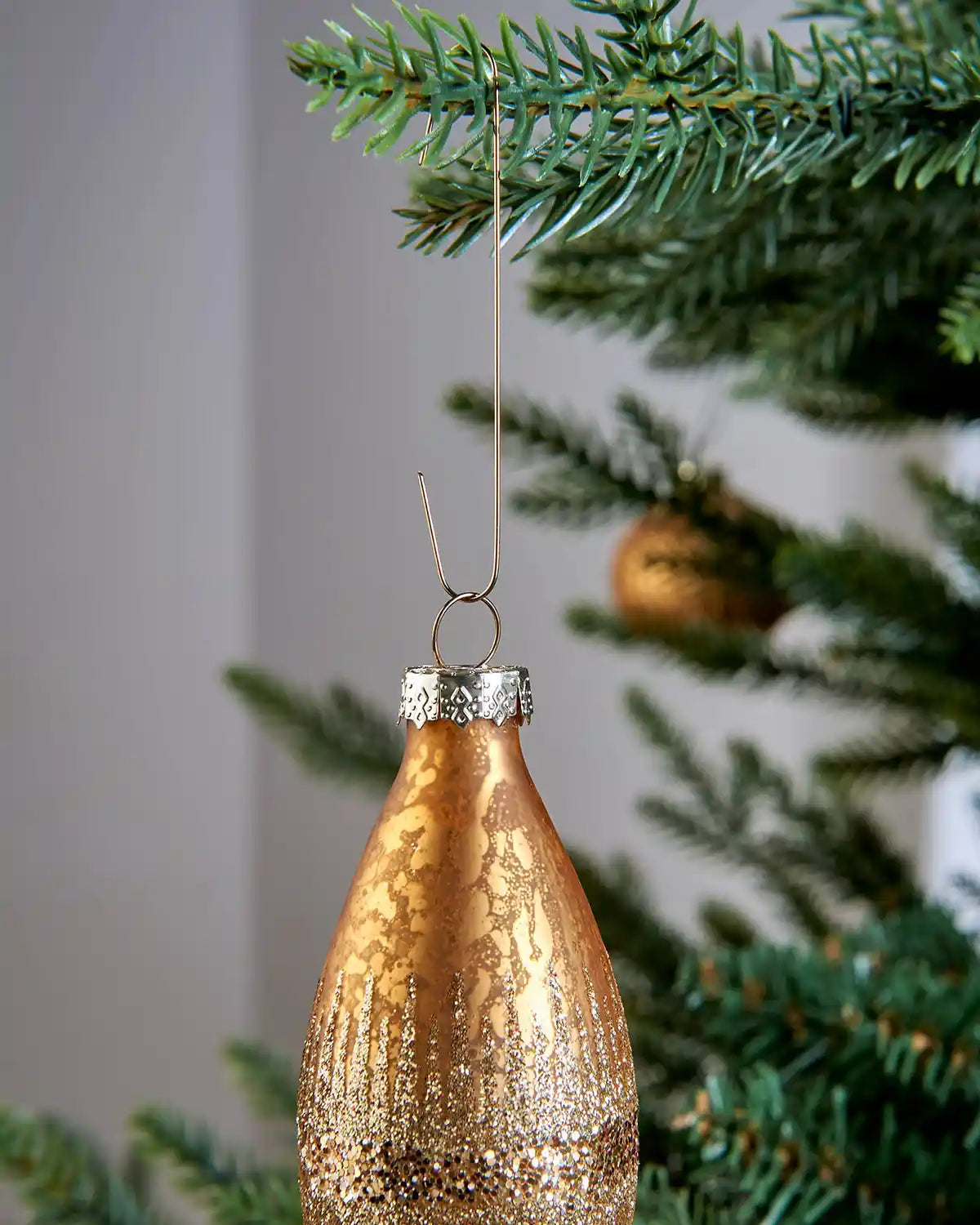 Gold ornament hook hanging a copper bauble from a Christmas tree branch