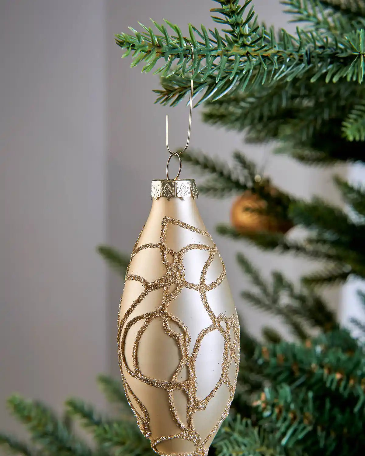 Gold ornament hook securing a cream and gold Christmas bauble to a tree branch