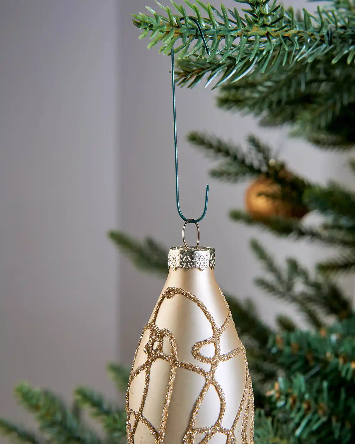 Cream Christmas ornament hanging from a green bauble hook on a tree branch