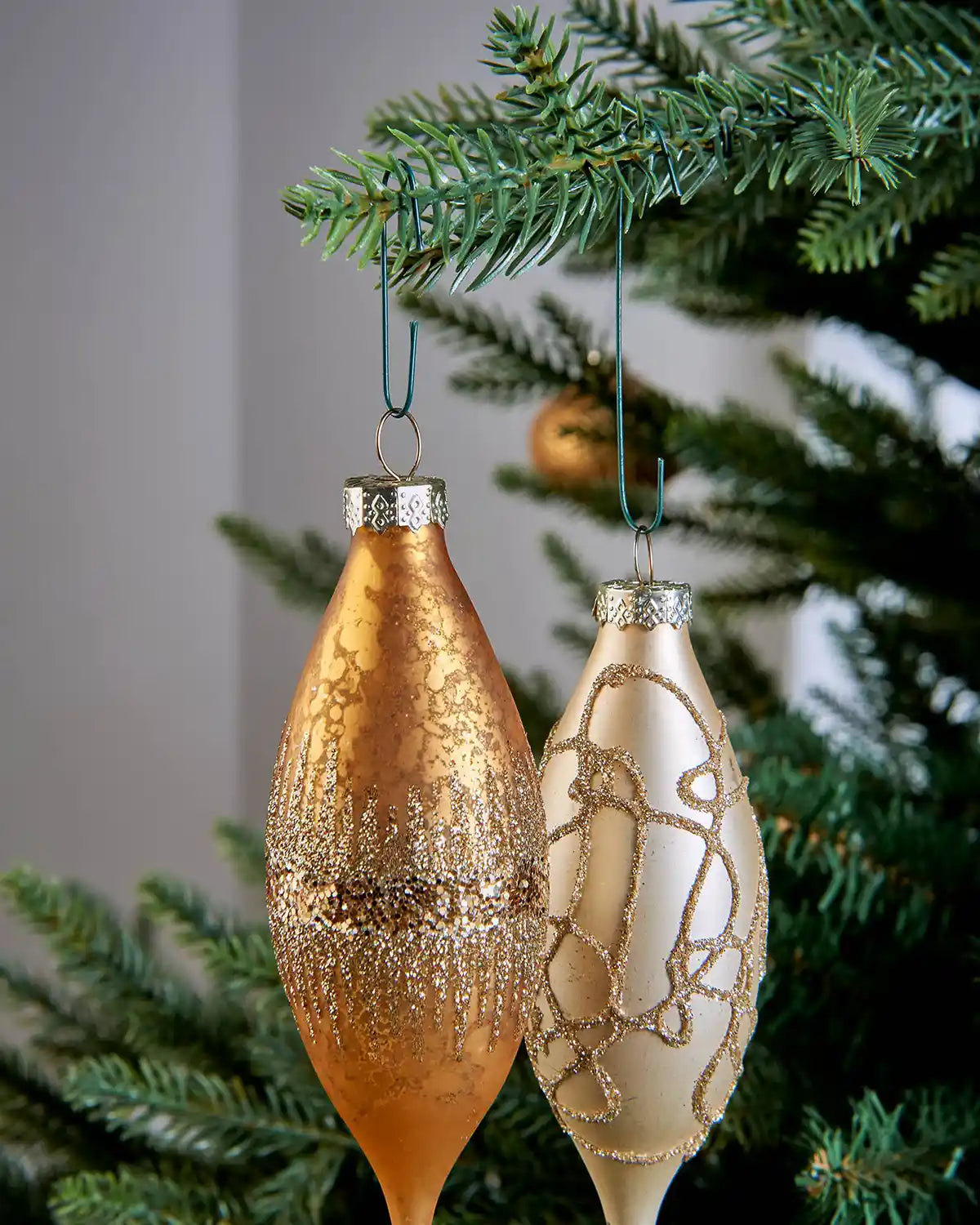Two Christmas ornaments hanging from green bauble hooks on a tree branch