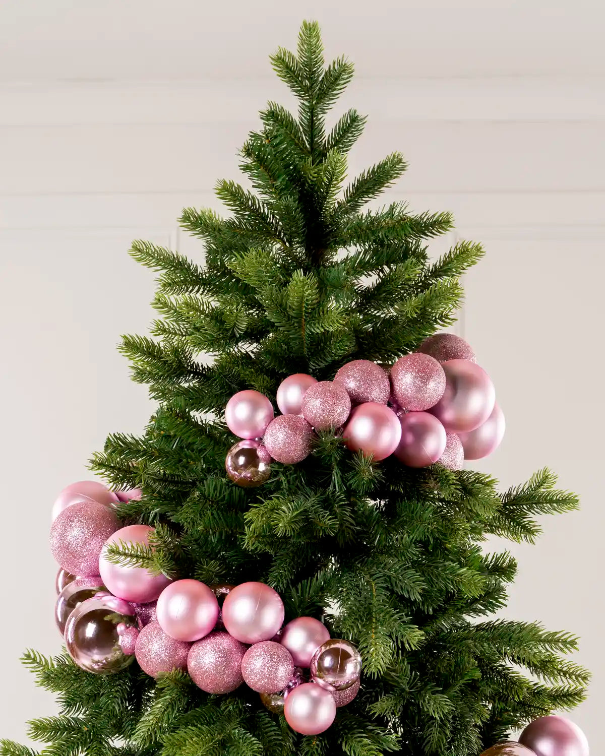 Pink bauble cluster arch arranged through the upper branches of a green Christmas tree.