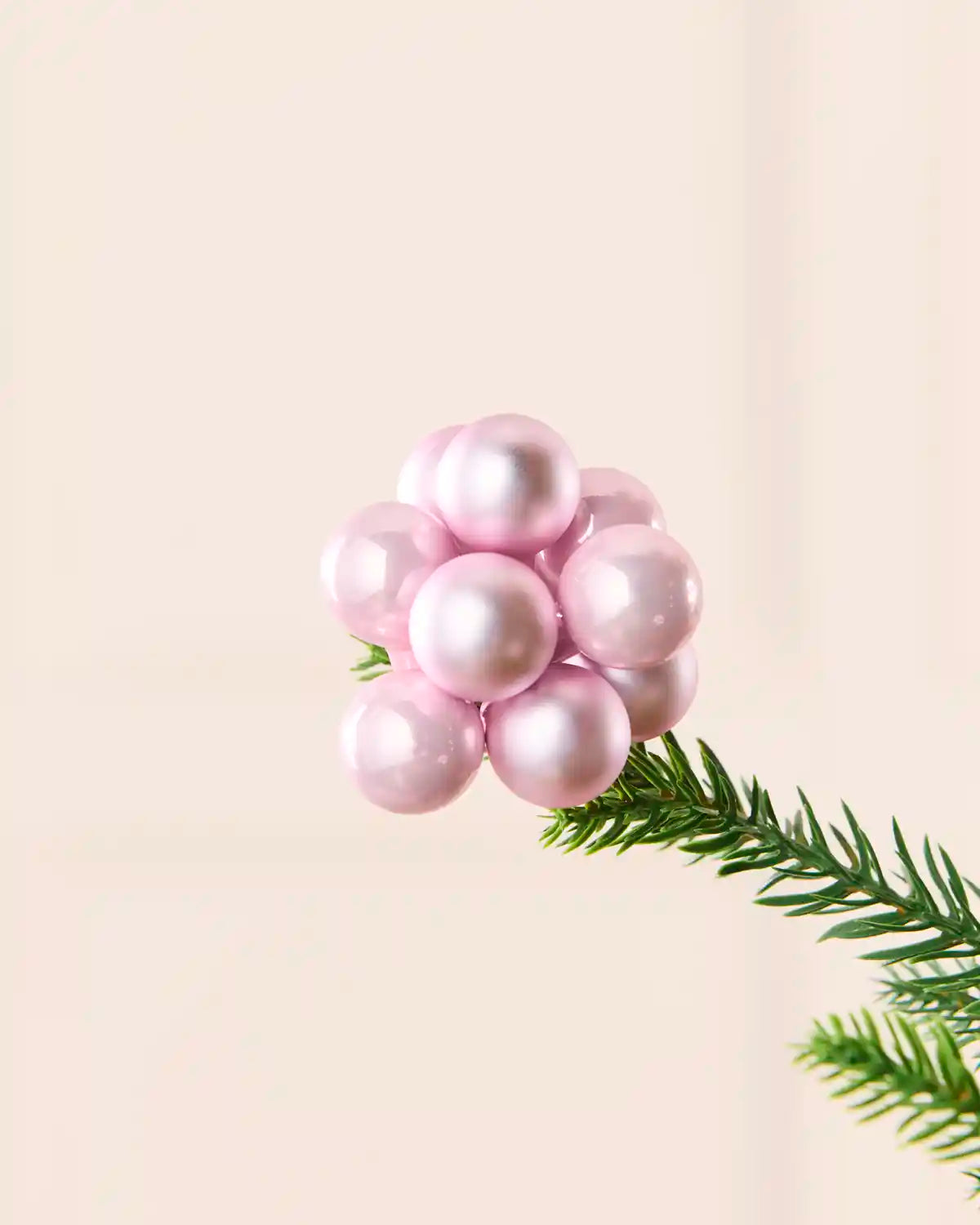 Close-up of a pink glass berry cluster bauble attached to a Christmas tree branch.
