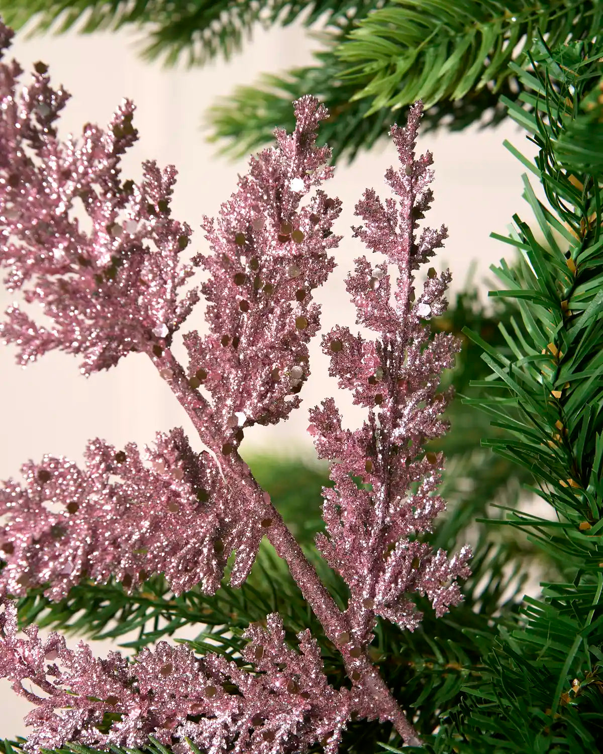 Close-up of a pink glitter leaf pick with sparkling sequin detail amongst Christmas tree foliage.