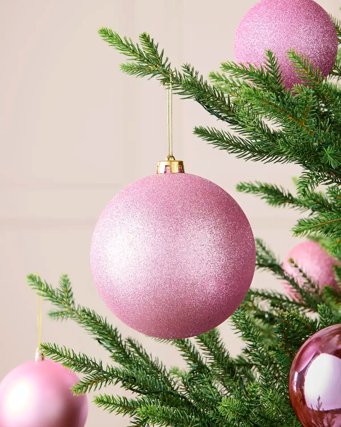 Glitter pink 15 cm shatterproof bauble displayed on a Christmas tree with coordinating pink matt and shiny baubles.