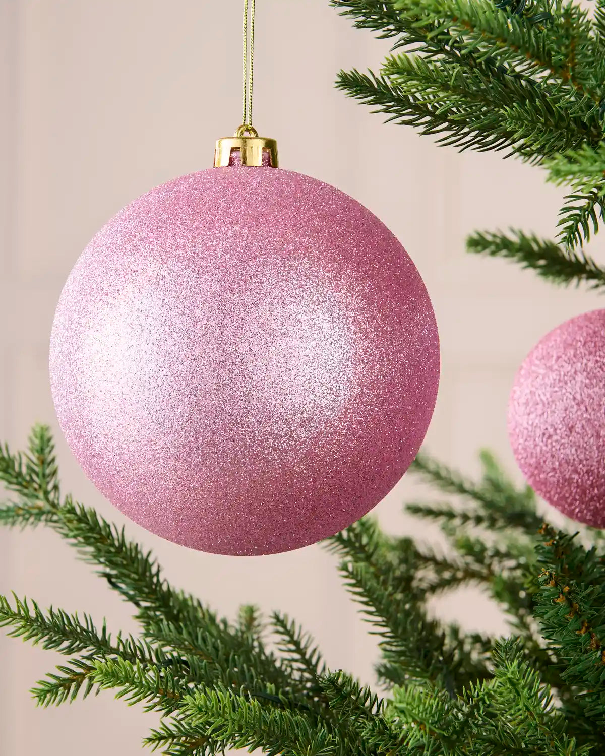 Close-up of an oversized 15 cm pink shatterproof bauble with a sparkling glitter finish on a Christmas tree.