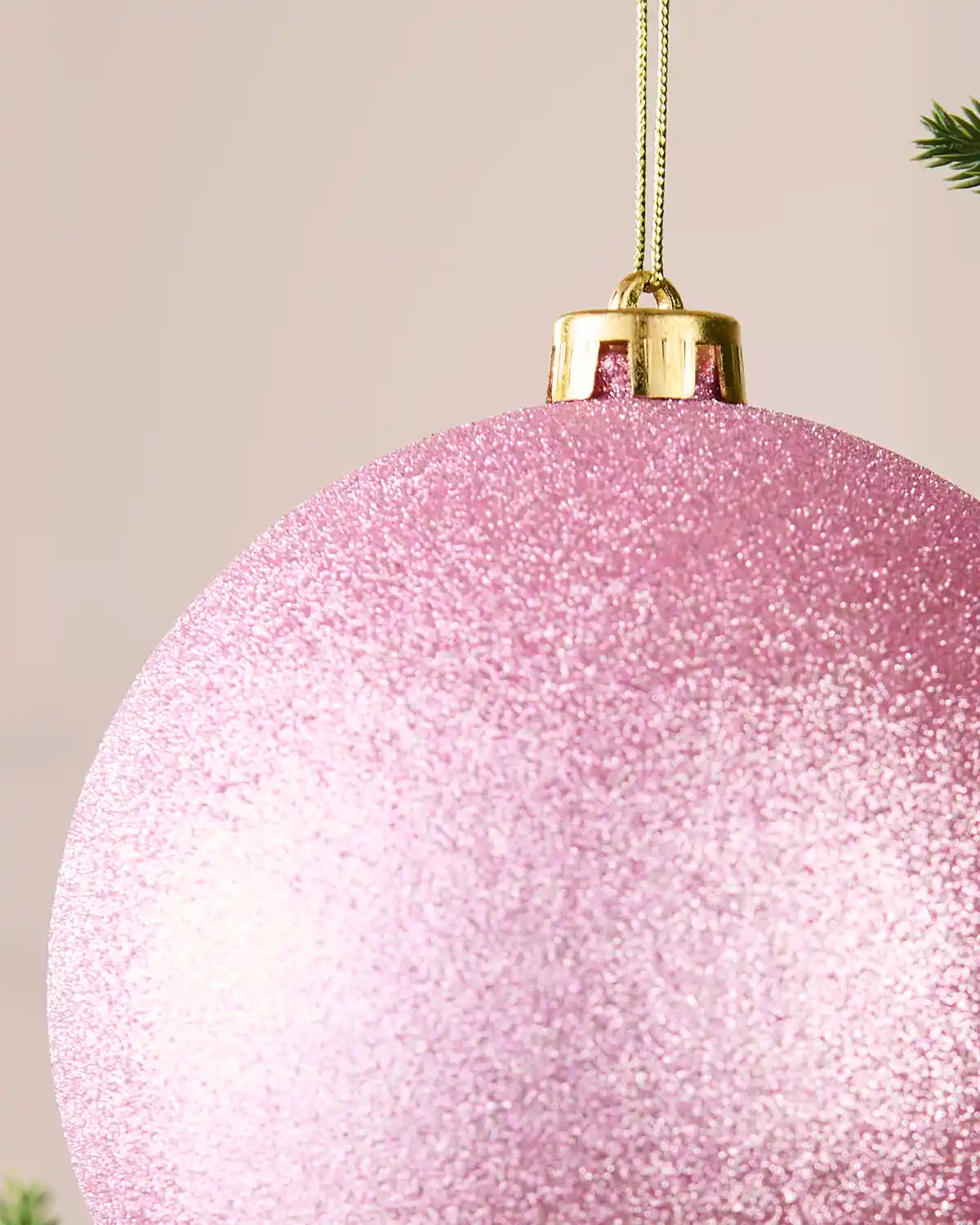 Detailed close-up of the glitter pink shatterproof bauble with its gold cap, hanging string and textured sparkle finish.