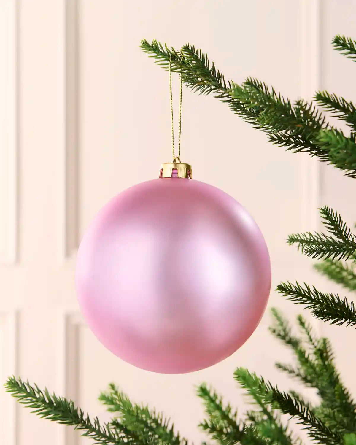 Pink 15 cm oversized shatterproof bauble with a smooth matt finish, gold cap and hanging string on a Christmas tree.