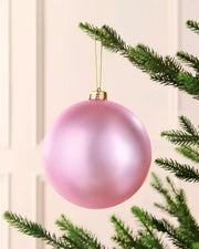 Pink 15 cm oversized shatterproof bauble with a smooth matt finish, gold cap and hanging string on a Christmas tree.