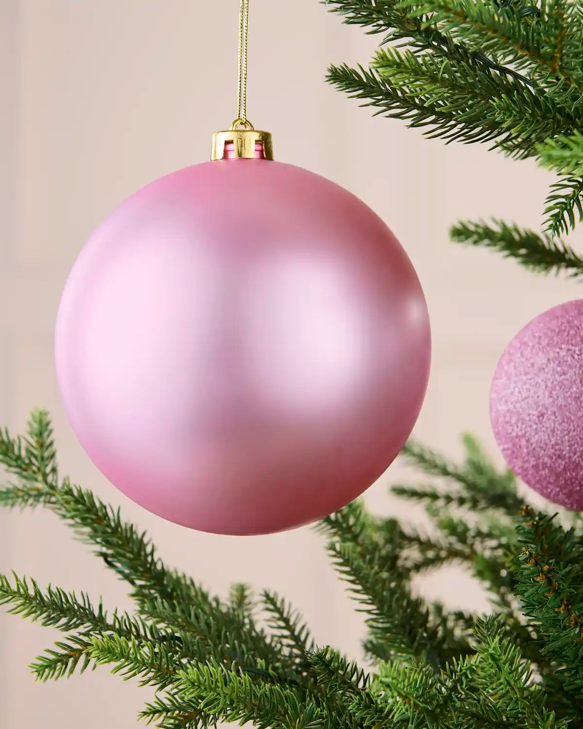 Close-up of an oversized 15 cm pink shatterproof bauble with a soft matt finish on a Christmas tree.