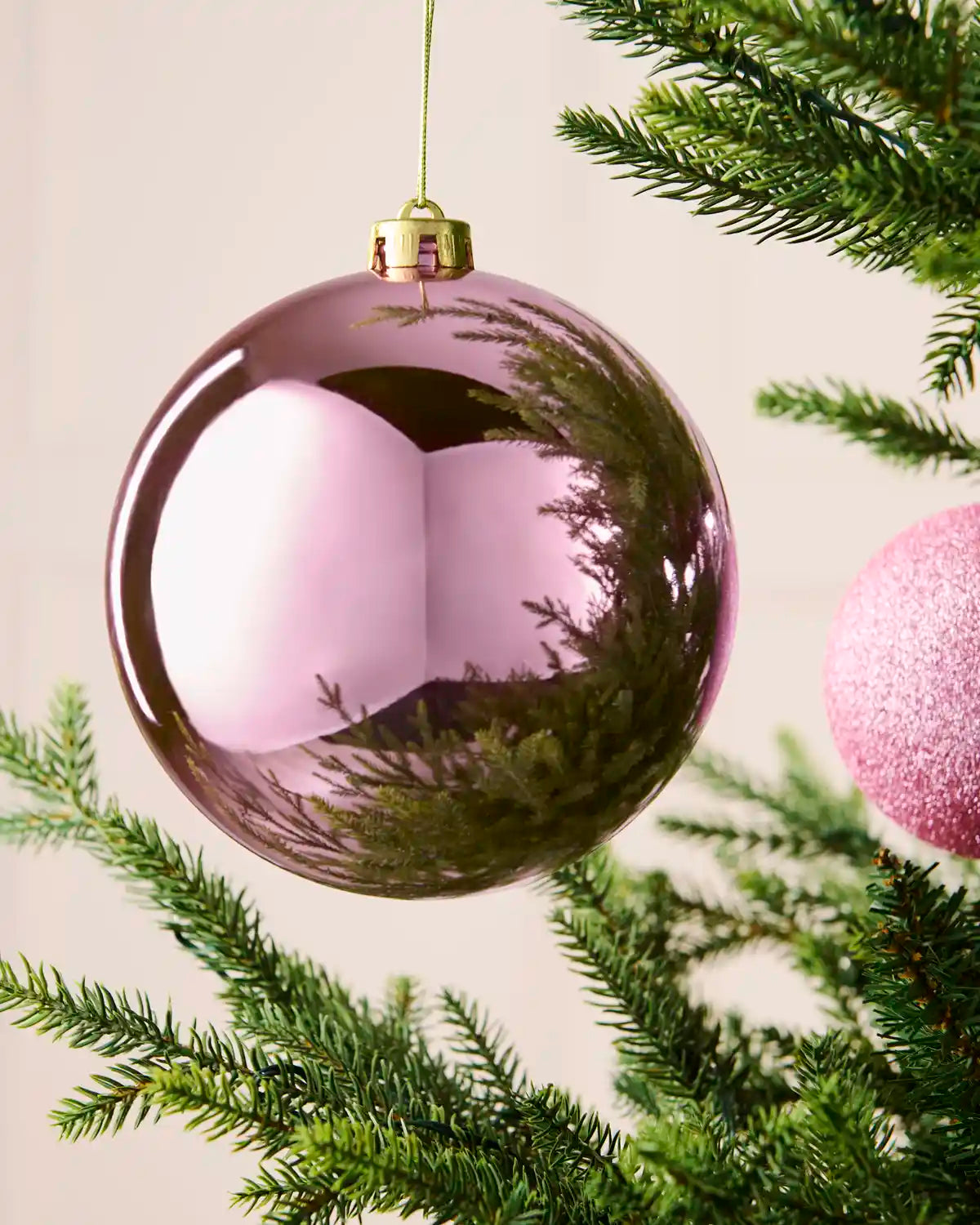 Close-up of a 15 cm oversized pink shatterproof bauble with a smooth shiny reflective finish on a Christmas tree.