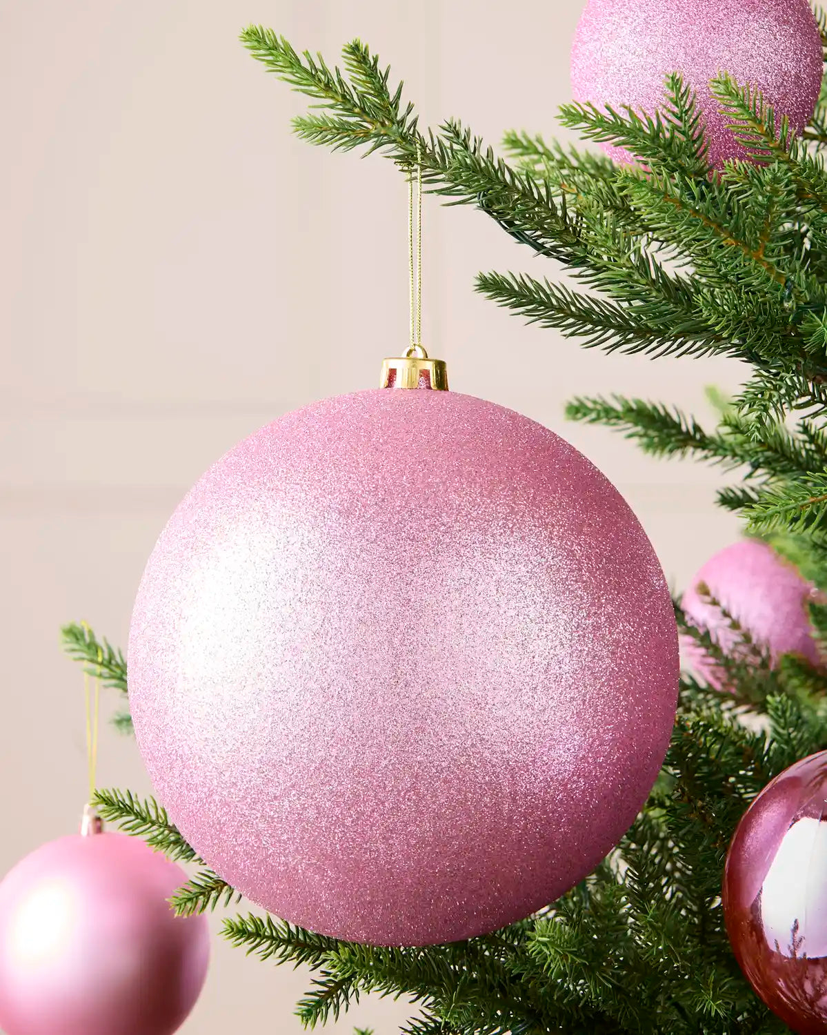 Oversized 20 cm pink glitter shatterproof bauble displayed on a Christmas tree with coordinating pink matt, glitter and shiny baubles.