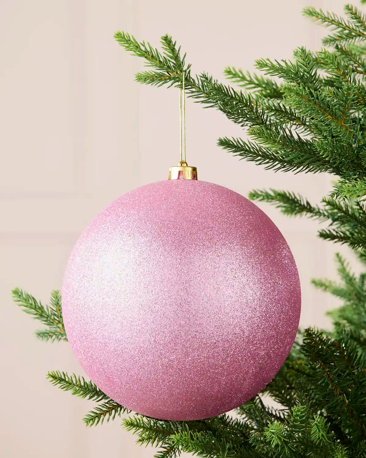 Pink 20 cm oversized shatterproof bauble with a glitter finish, gold cap and hanging string displayed on a Christmas tree.