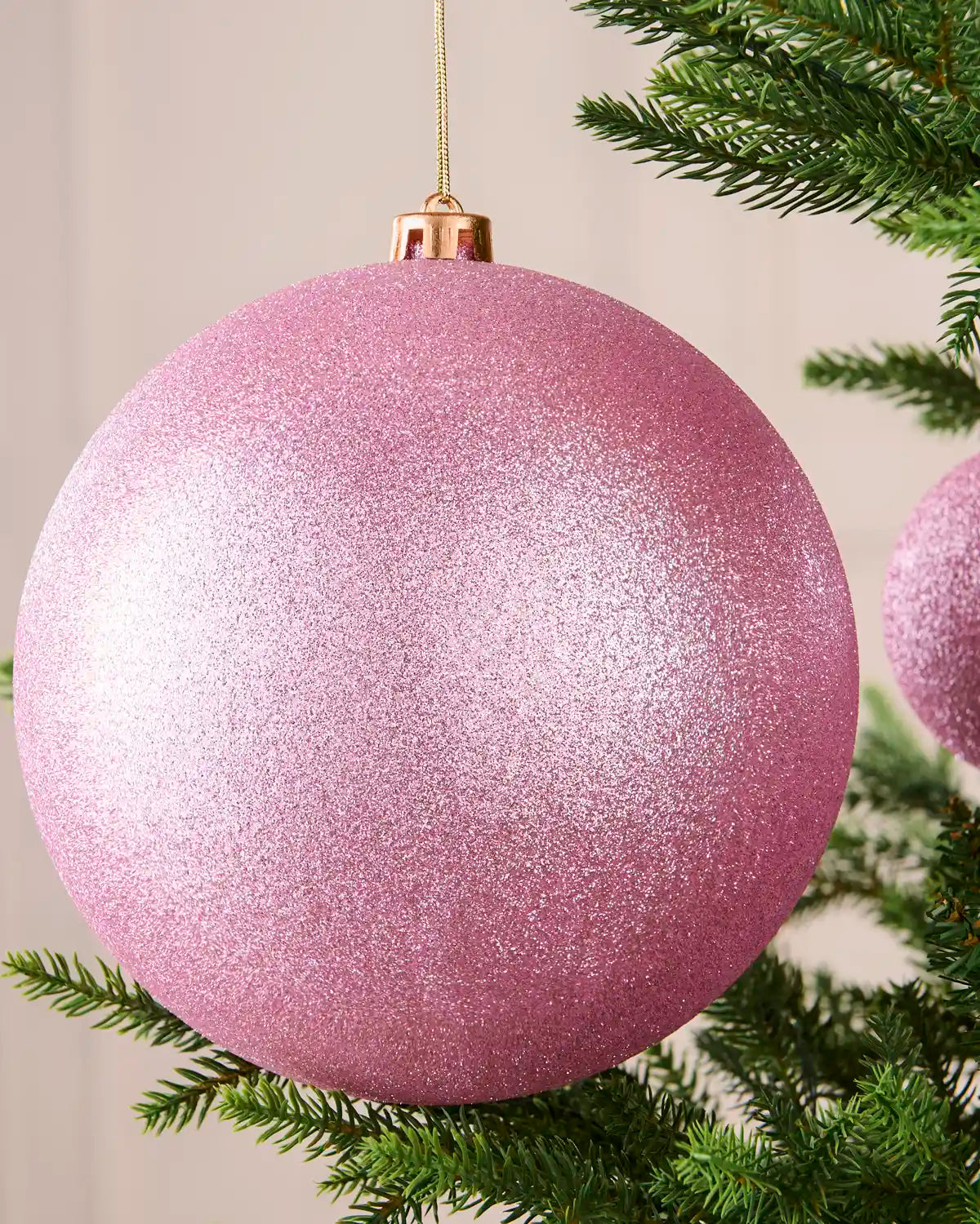 Close-up of a 20 cm oversized pink shatterproof bauble with a glitter finish hanging on a Christmas tree.