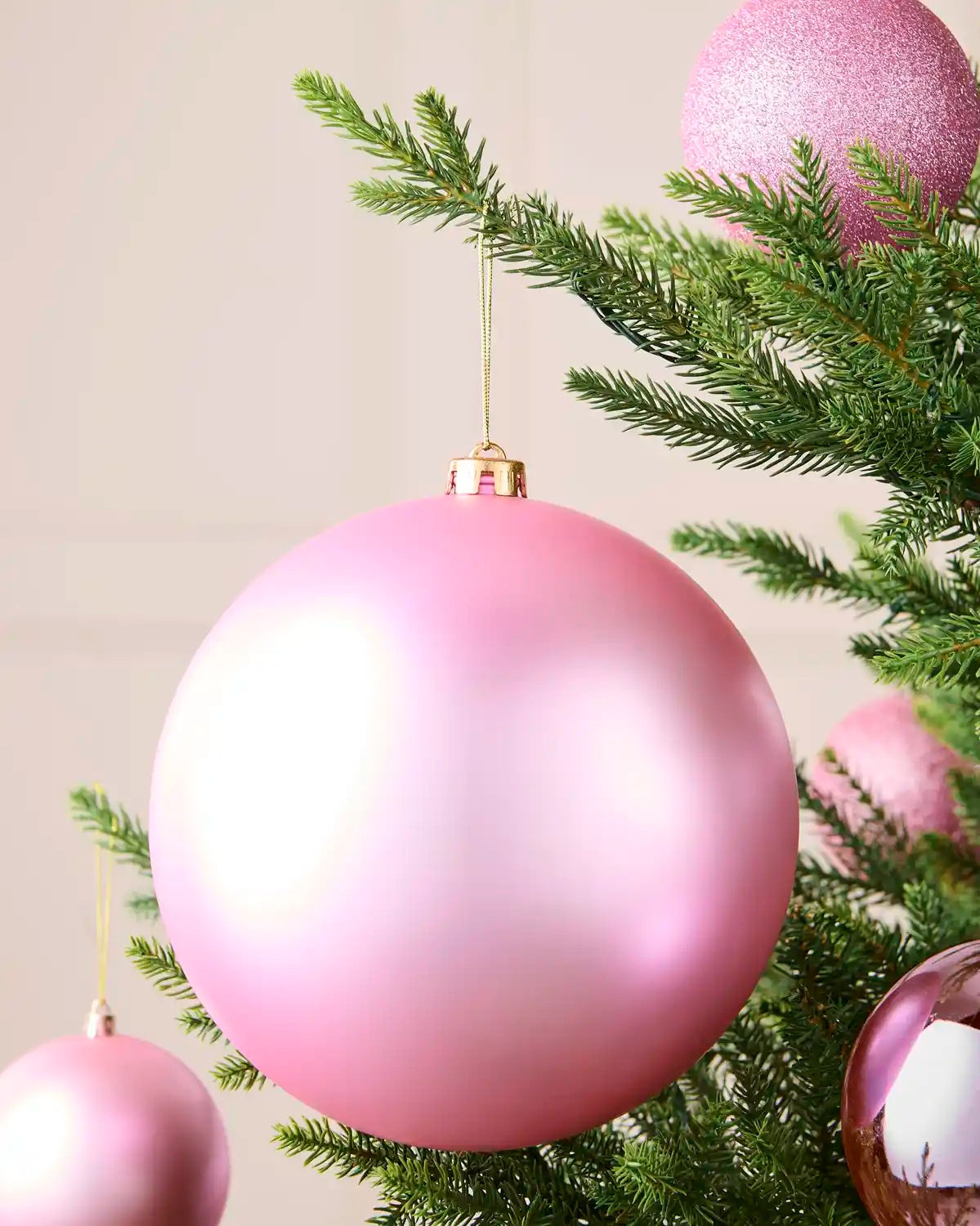Matt pink 20 cm shatterproof bauble displayed on a Christmas tree with coordinating pink glitter and shiny baubles.