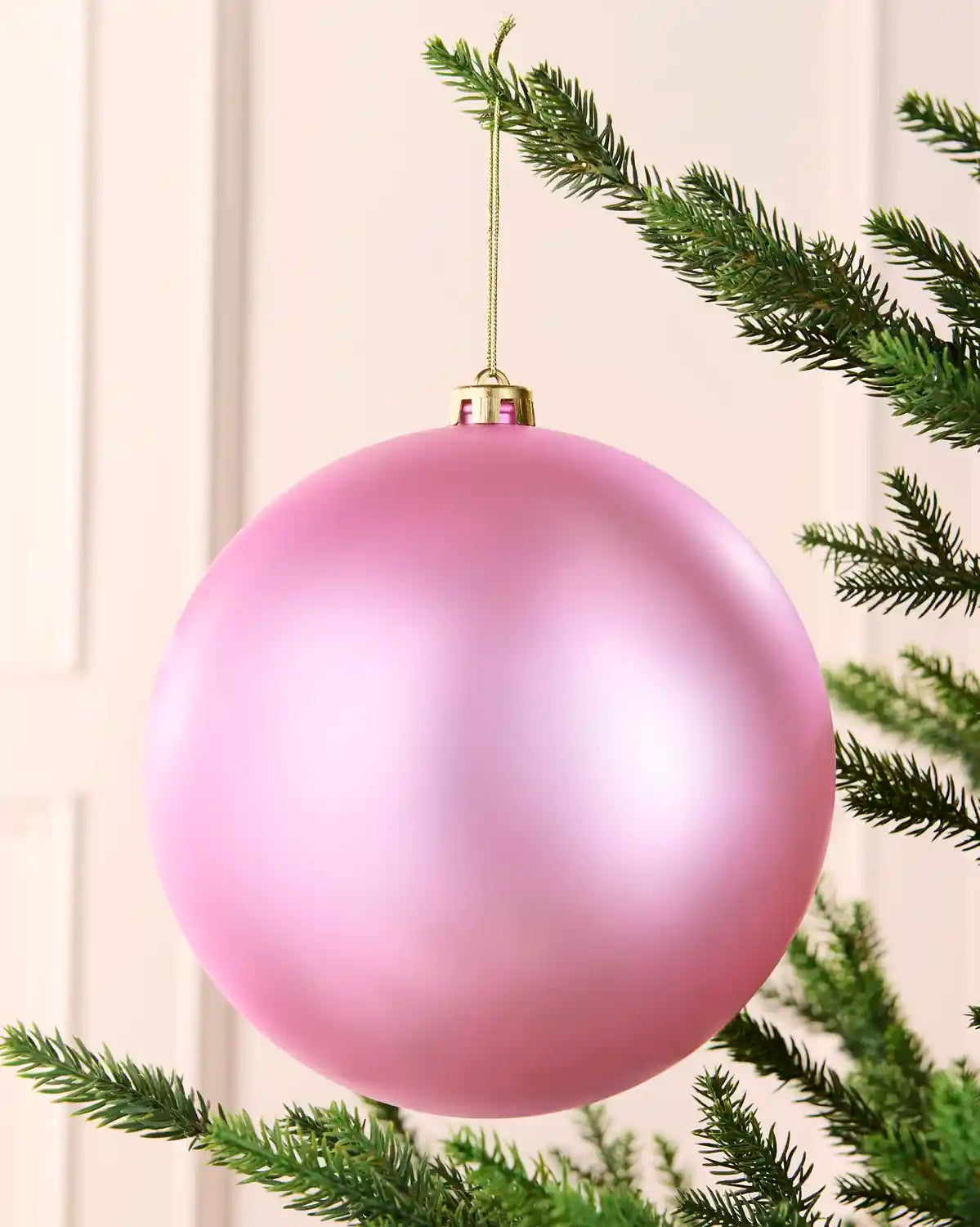 Pink 20 cm oversized shatterproof bauble with a smooth matt finish, gold cap and hanging string on a Christmas tree.