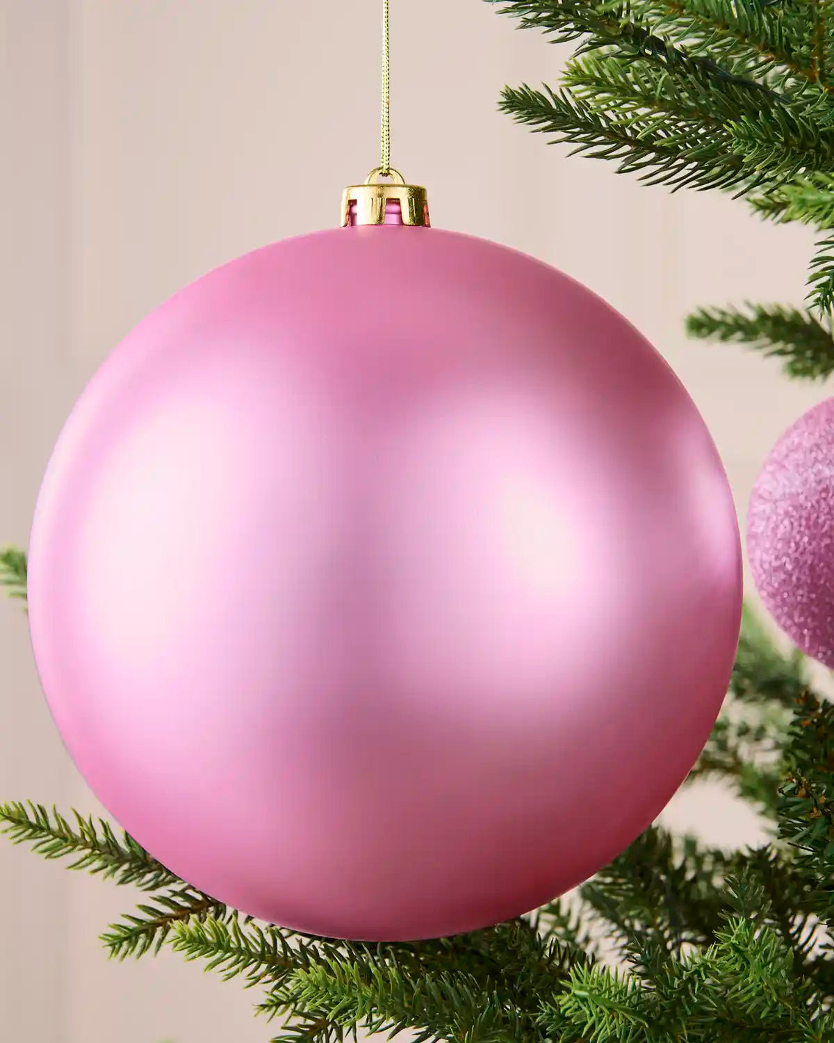 Close-up of an oversized 20 cm pink shatterproof bauble with a soft matt finish on a Christmas tree.