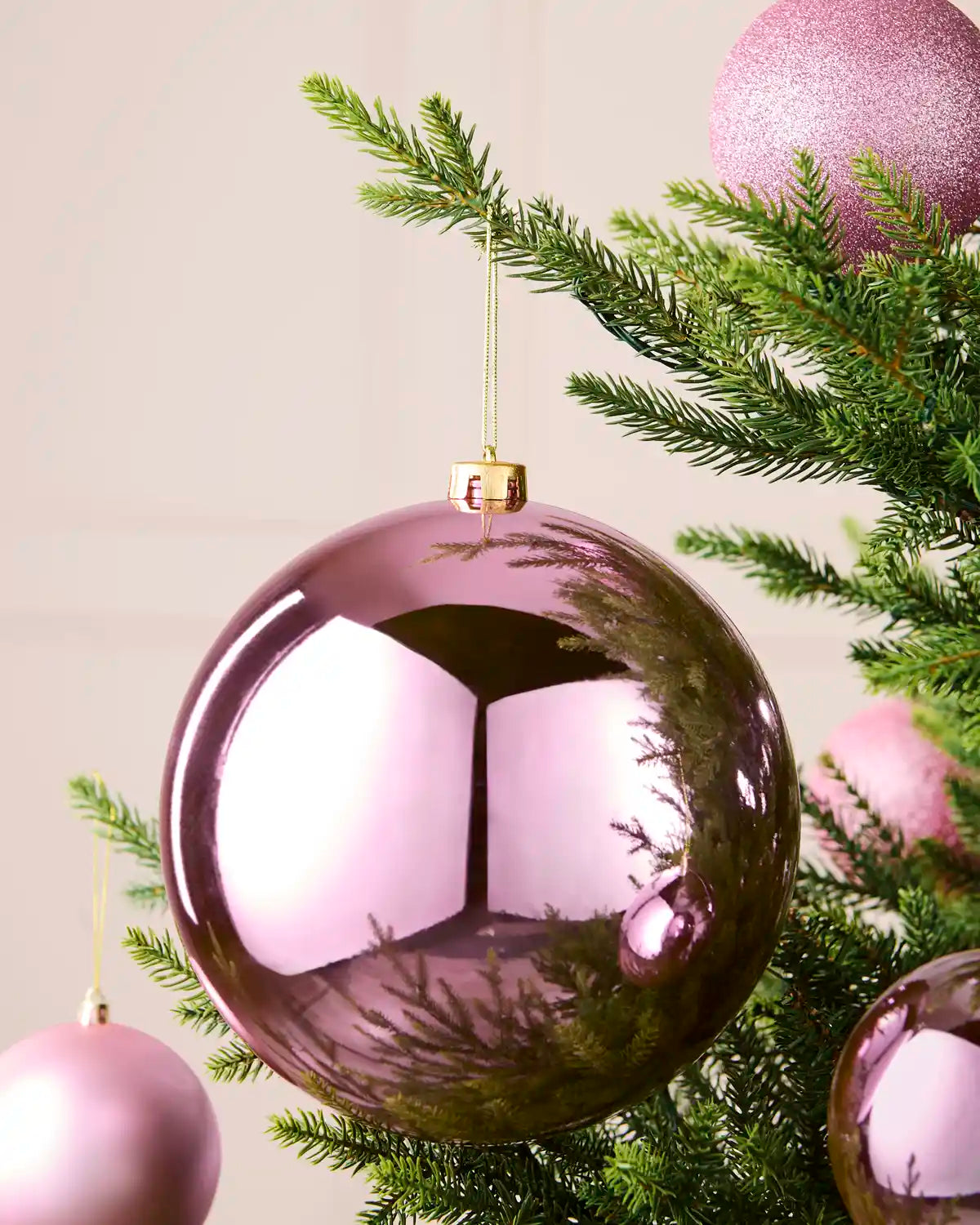 Shiny pink 20 cm shatterproof bauble displayed on a Christmas tree with coordinating pink matt and glitter baubles.