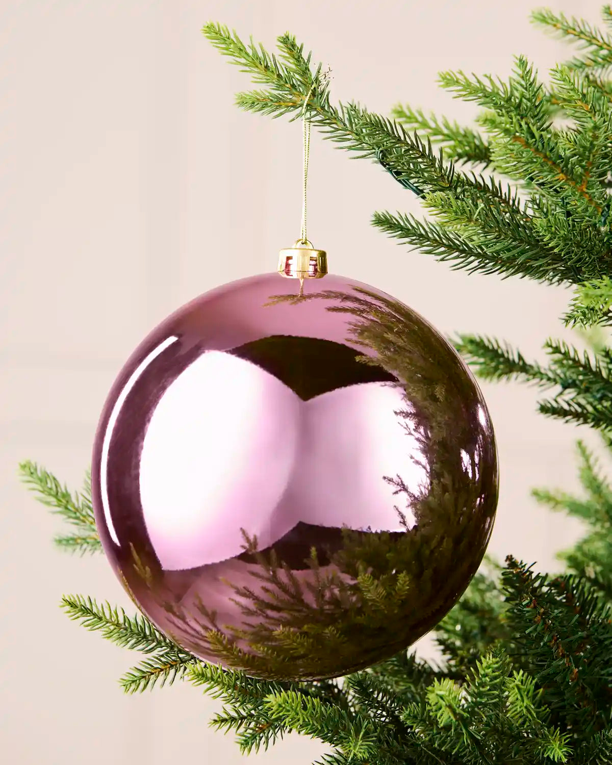 Pink 20 cm oversized shatterproof bauble with a shiny reflective finish, gold cap and hanging string on a Christmas tree.