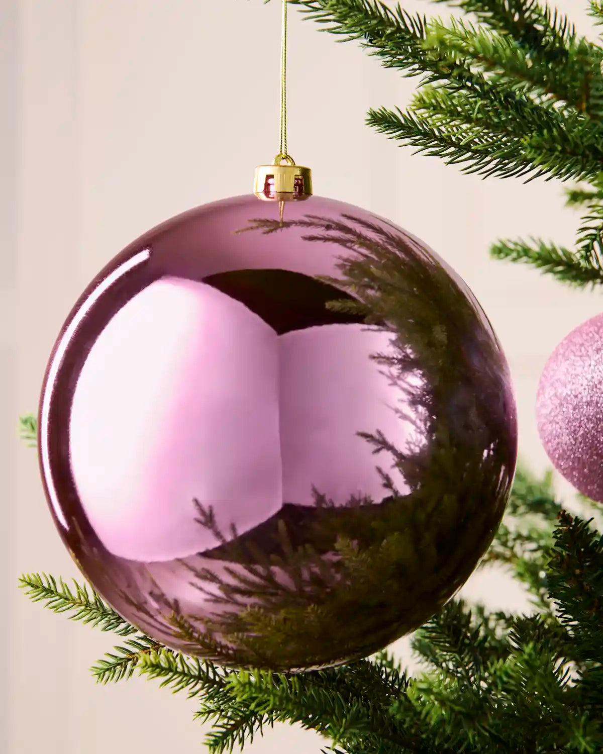 Close-up of an oversized 20 cm pink shatterproof bauble with a smooth, shiny reflective finish on a Christmas tree.