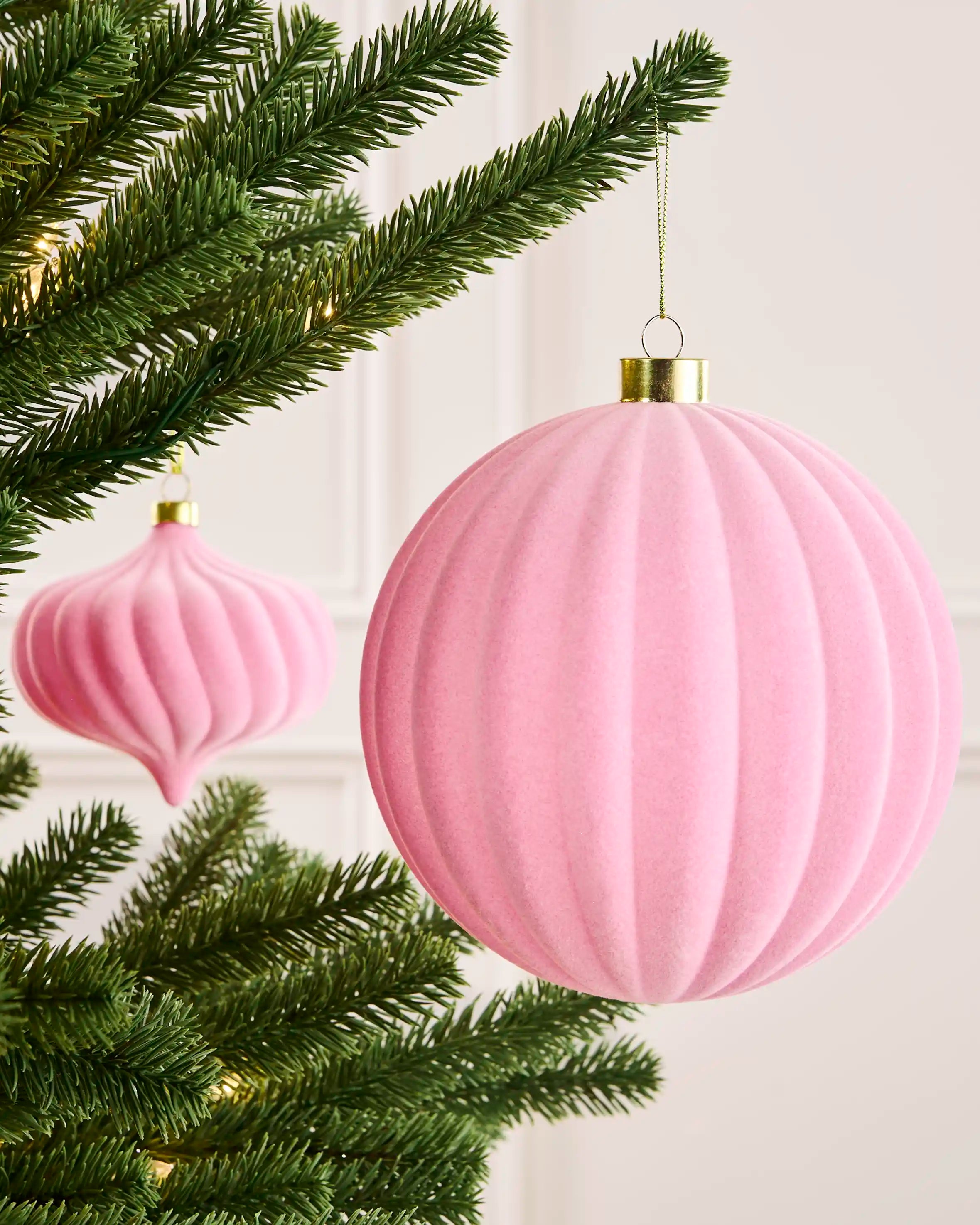 Pink 15 cm ribbed velvet bauble hanging from a Christmas tree, with a matching spiral bauble visible behind.