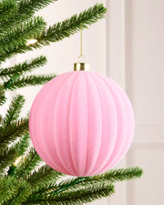 Pink 15 cm oversized velvet bauble with a ribbed round design, gold cap and hanging string on a Christmas tree.