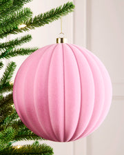 20 cm pink oversized velvet ribbed bauble hanging on a Christmas tree with a gold cap and hanging string.