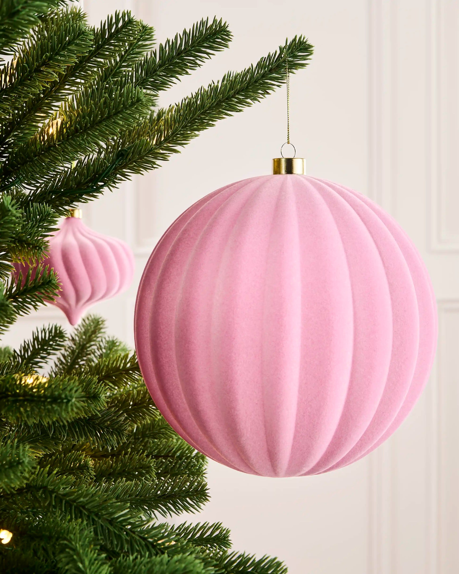 Pink 20 cm oversized velvet ribbed bauble displayed on a Christmas tree with a coordinating pink ornament behind.