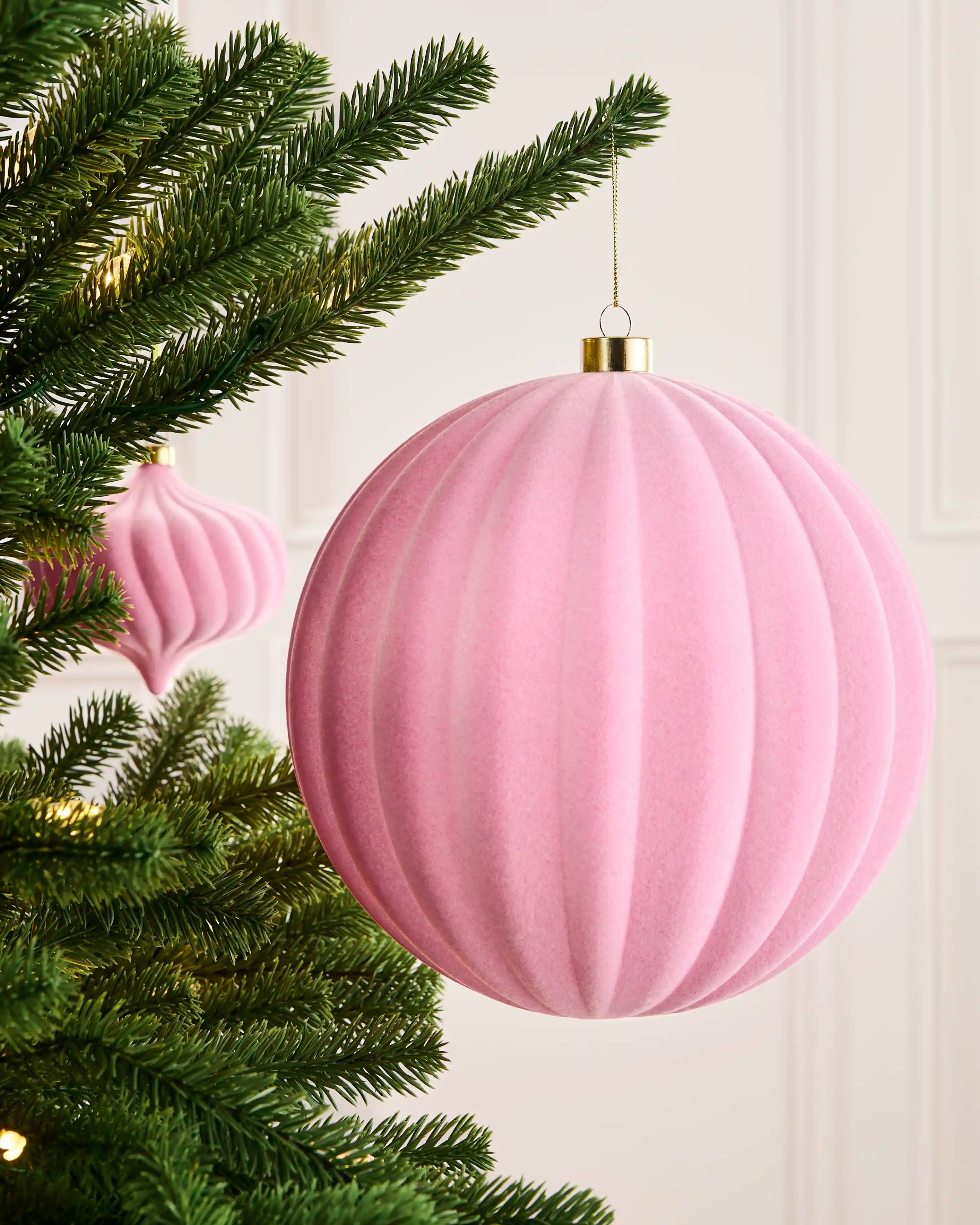 Pink 20 cm oversized velvet ribbed bauble displayed on a Christmas tree with a coordinating pink ornament behind.