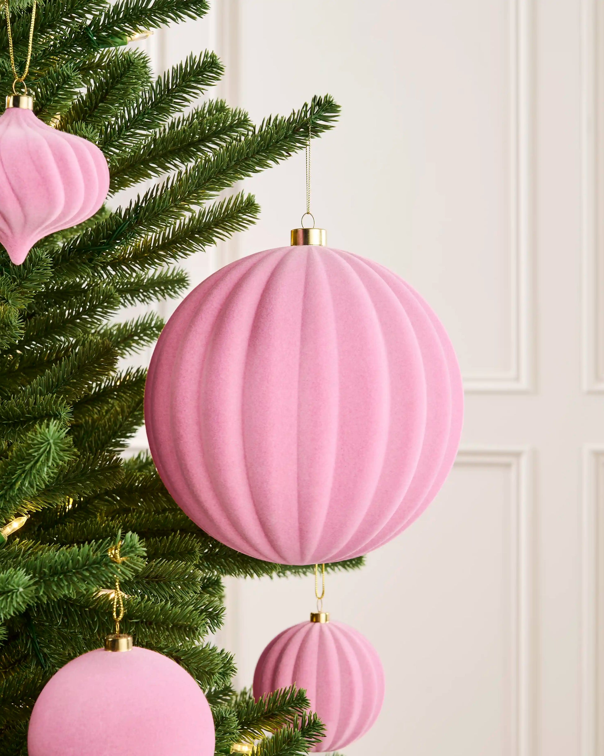 Large pink 20 cm oversized velvet ribbed bauble styled on a Christmas tree with coordinating pink ornaments.