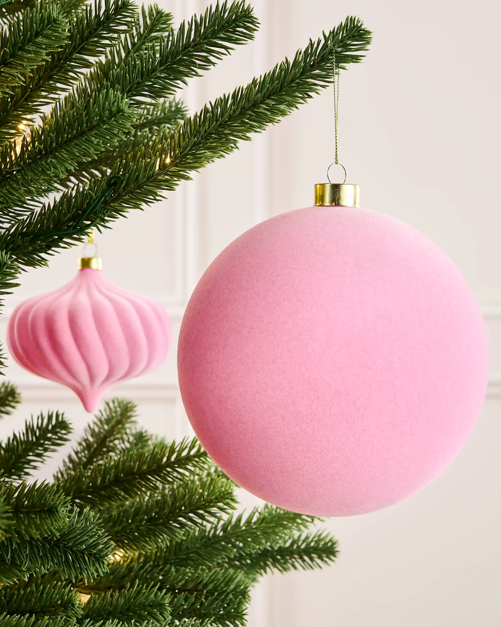 Pink 15 cm traditional velvet bauble hanging from a Christmas tree, with a matching shaped bauble visible behind.