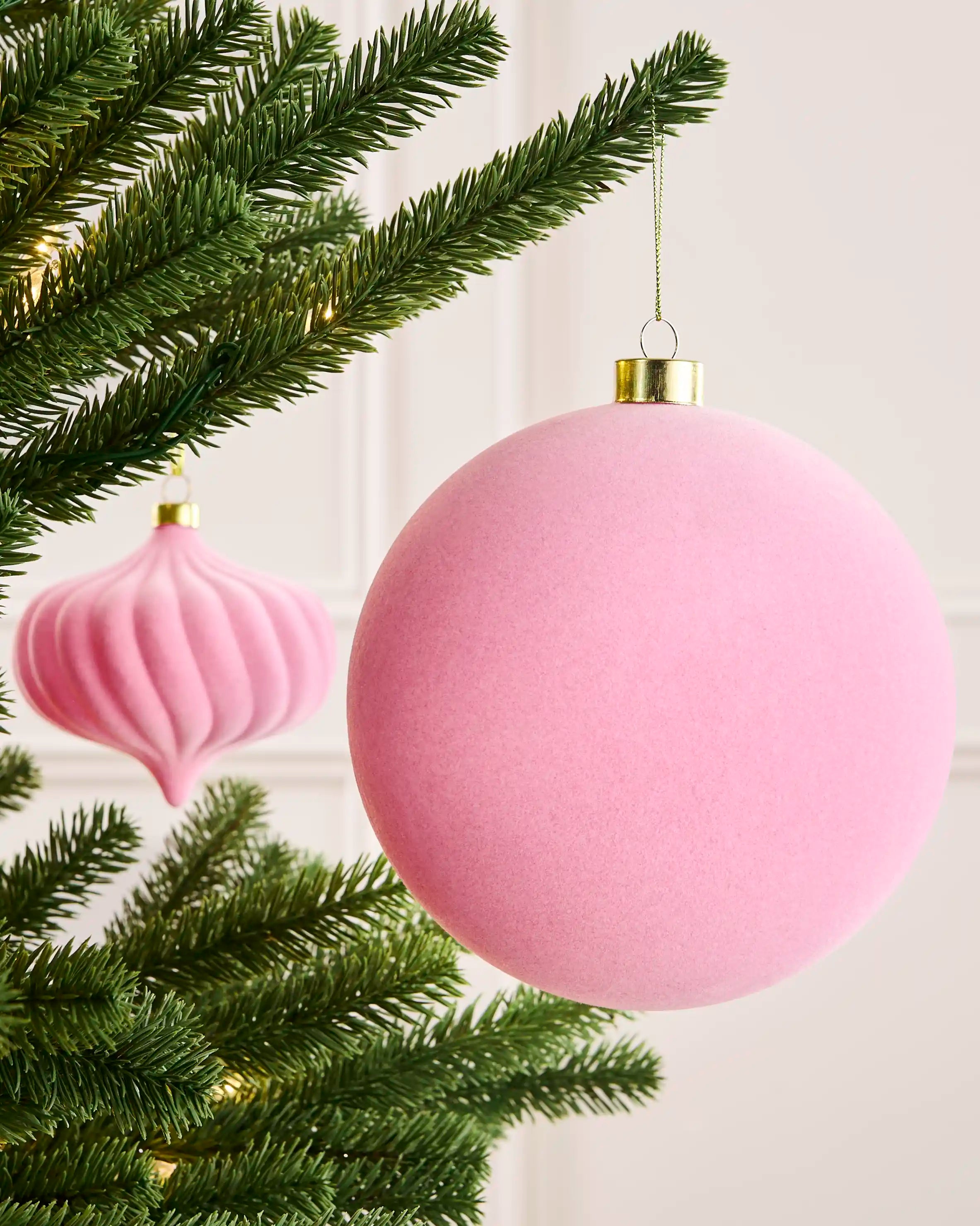 Pink 15 cm traditional velvet bauble hanging from a Christmas tree, with a matching shaped bauble visible behind.