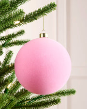 Pink 15 cm oversized velvet bauble with a traditional round shape, gold cap and hanging string on a Christmas tree.