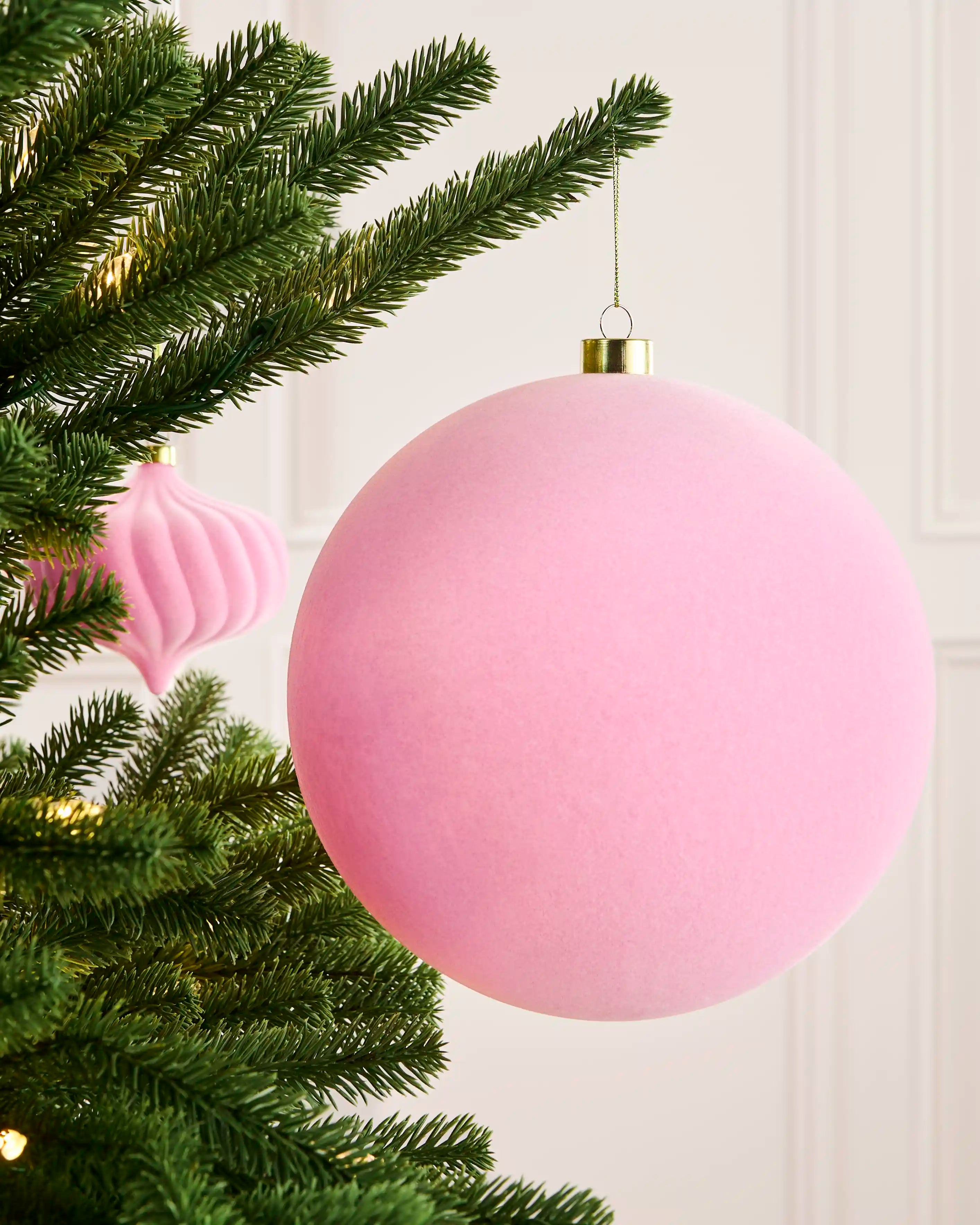 Pink 20 cm oversized velvet traditional bauble displayed on a Christmas tree with a coordinating pink ornament behind.