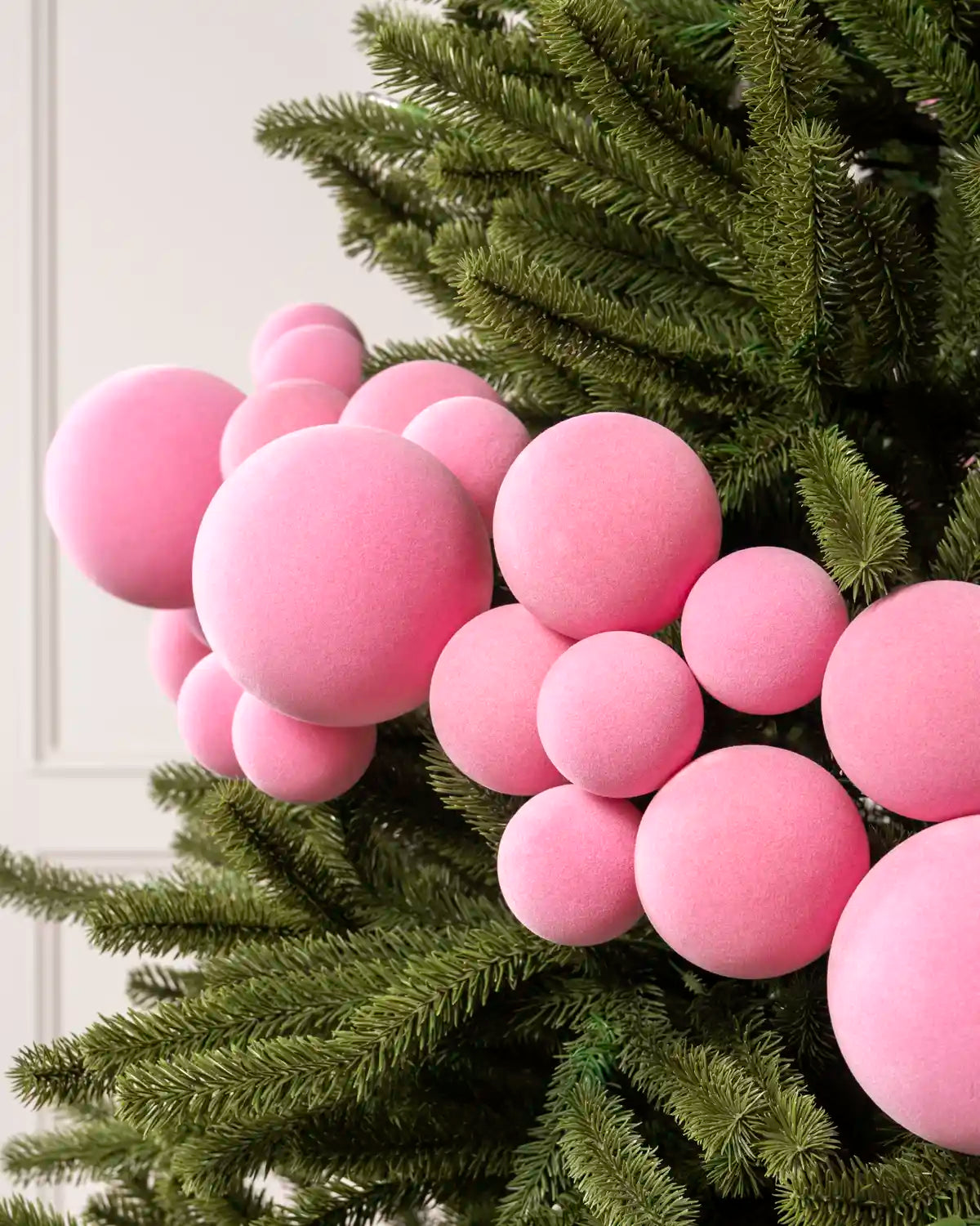 Close-up of pink velvet bauble garland on a Christmas tree showing the soft textured finish and mixed bauble sizes.