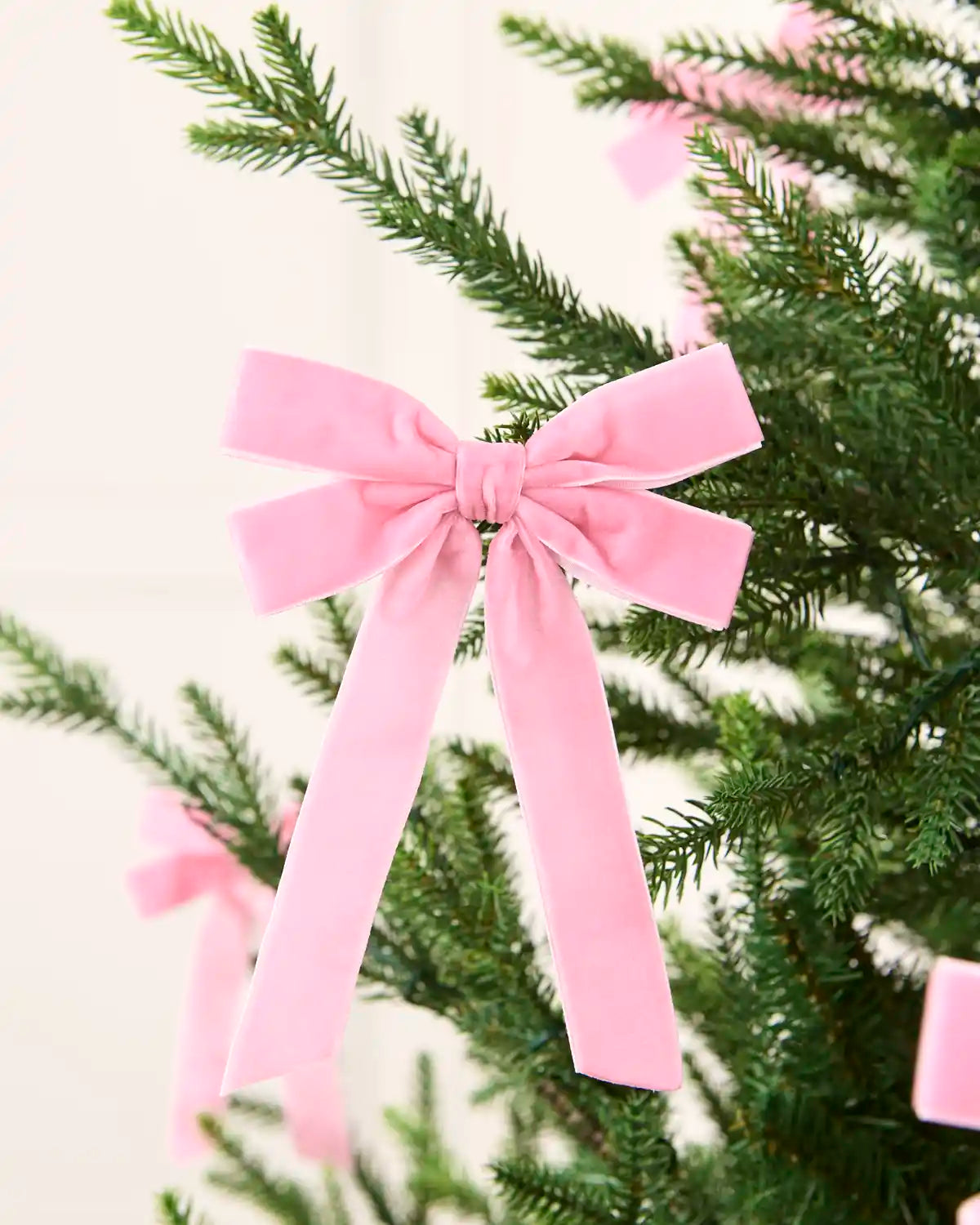 Pink velvet double bow displayed among matching bows on a Christmas tree.