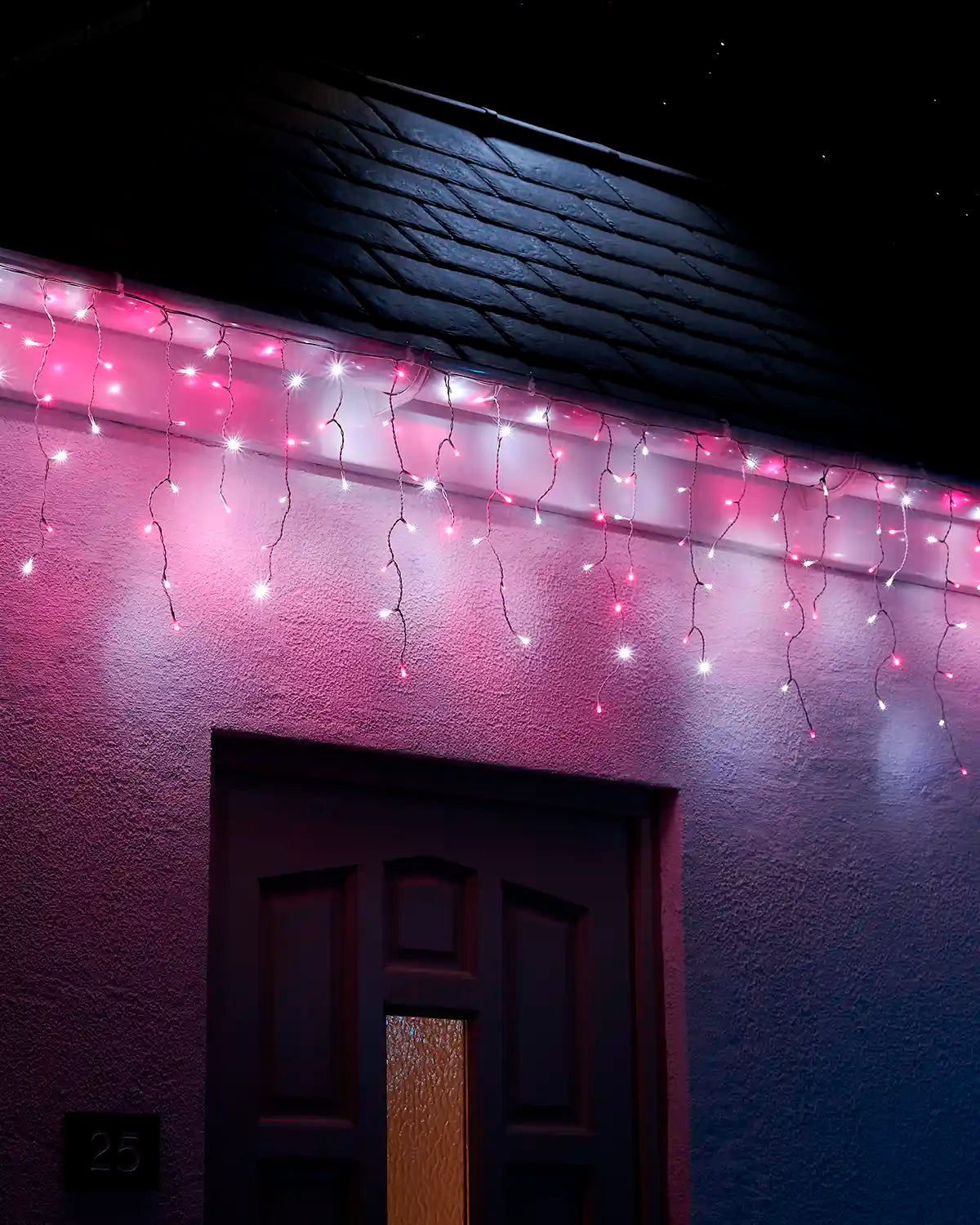 Pink and white icicle lights with white cable displayed along a roofline above a front door at night.
