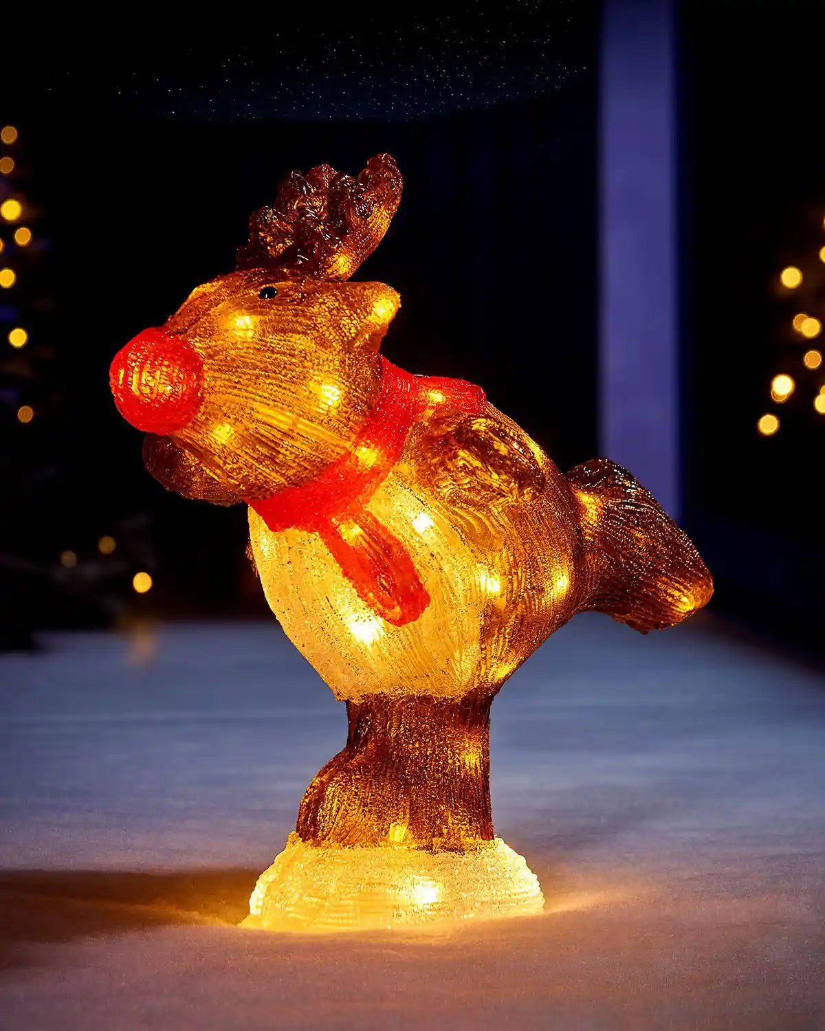 Pre-lit acrylic reindeer figurine glowing outdoors with warm festive lights in the background