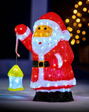 Pre-lit acrylic Santa figurine glowing outdoors with a lantern and festive lights in the background